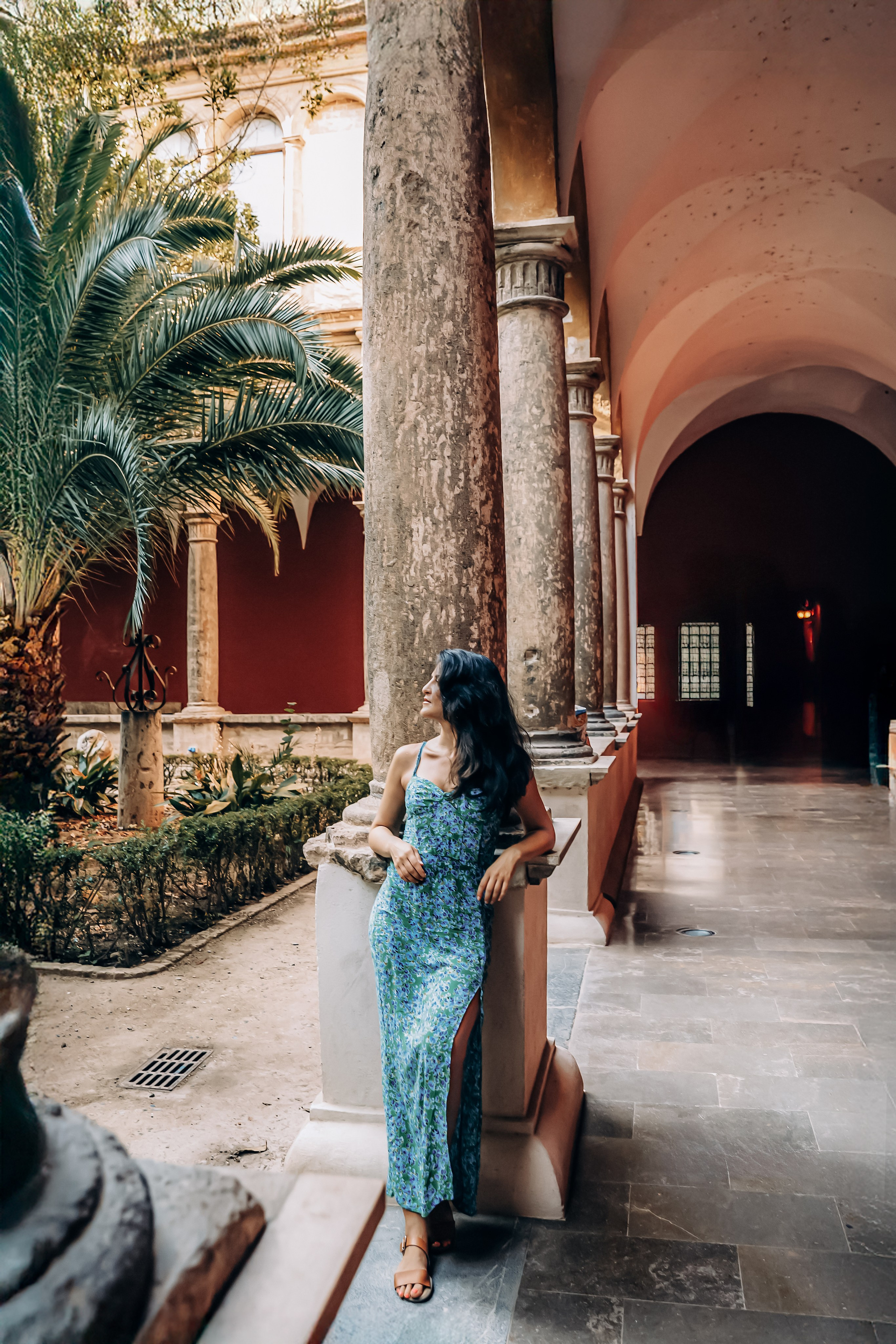 Женская фотосессия в Валенсии, Испания, с элегантной женщиной в струящемся платье среди исторических арок, каменных колонн и пальм, снятая в тёплом естественном свете — идеально для женской портретной фотографии, лайфстайл-съёмок, художественных редакционных портретов и вневременных женских фотосессий в Валенсии и по всей Испании.