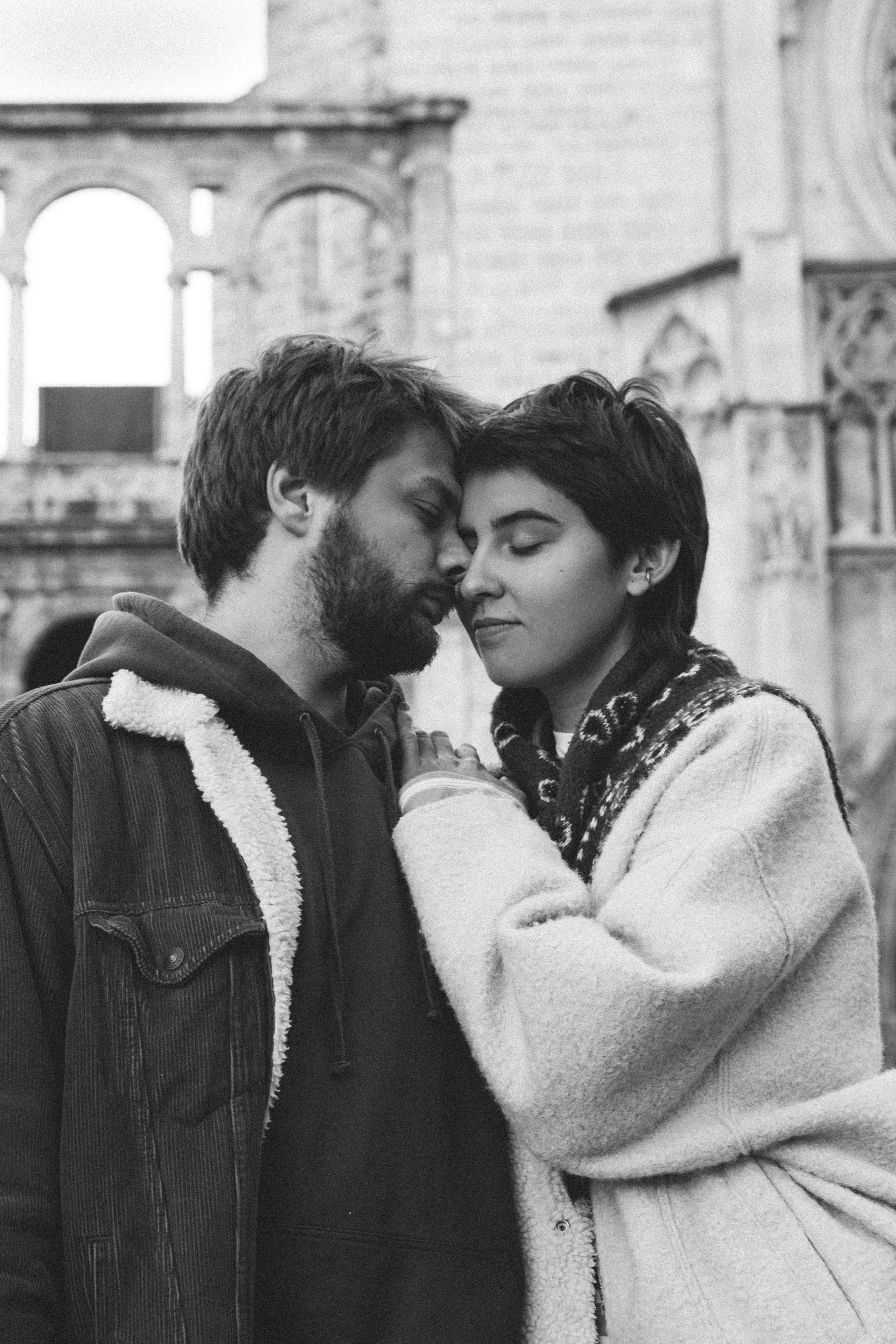 Intimate black and white portrait of a couple embracing tenderly in front of the historic Gothic architecture of Valencia Cathedral, capturing a quiet romantic moment in the heart of Valencia, Spain.