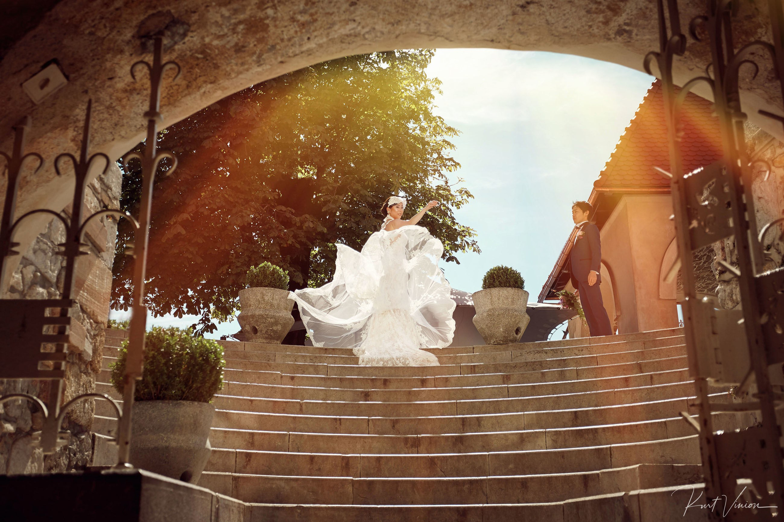 Bride lifting gown in dramatic sunflare Bled Castle courtyard.