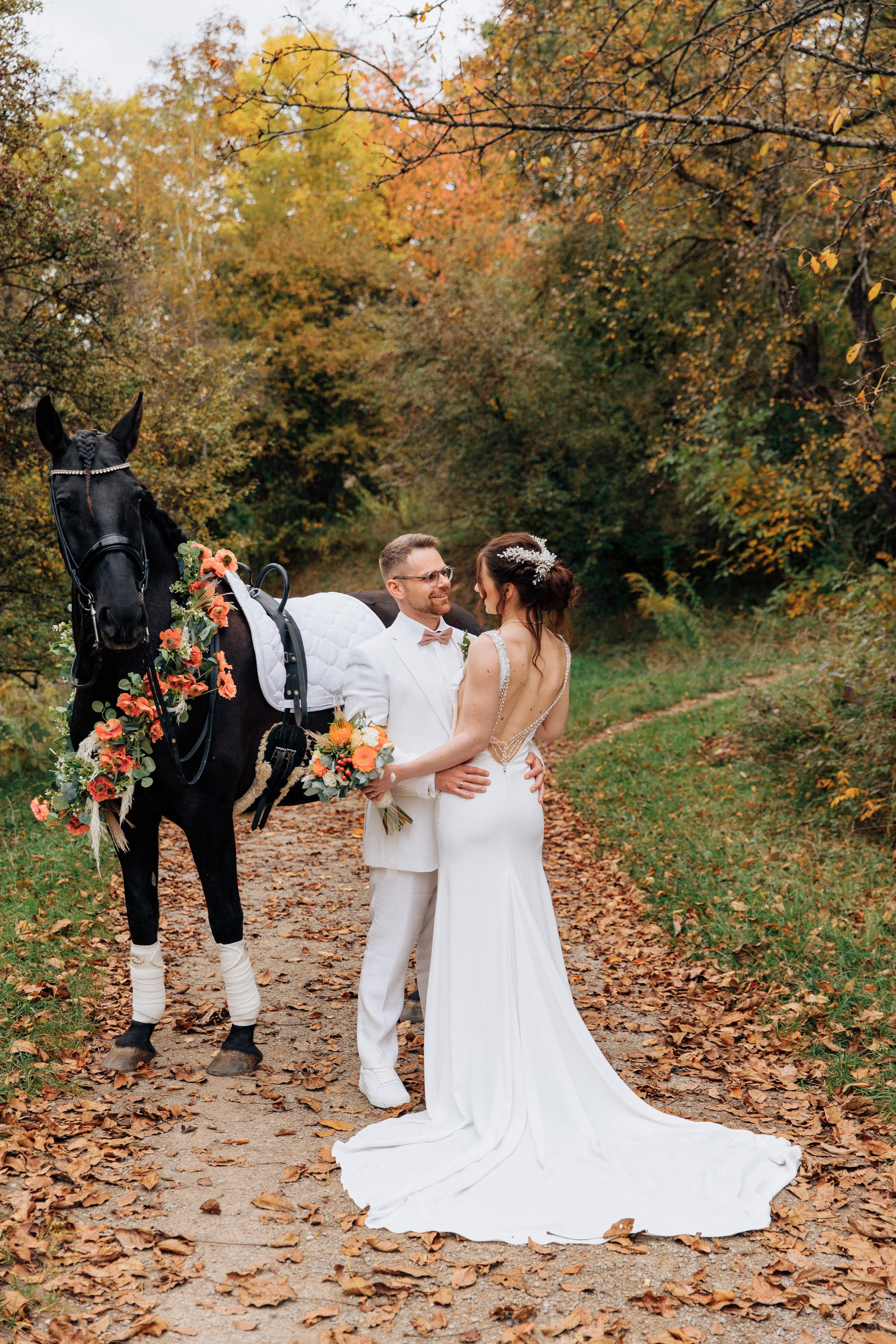 Der Bräutigam umarmt die Braut, die mit dem Rücken zu uns steht und ihr Hochzeitskleid zeigt, neben ihnen ein Pferd. Perfekte Hochzeitsfotos des Brautpaares.