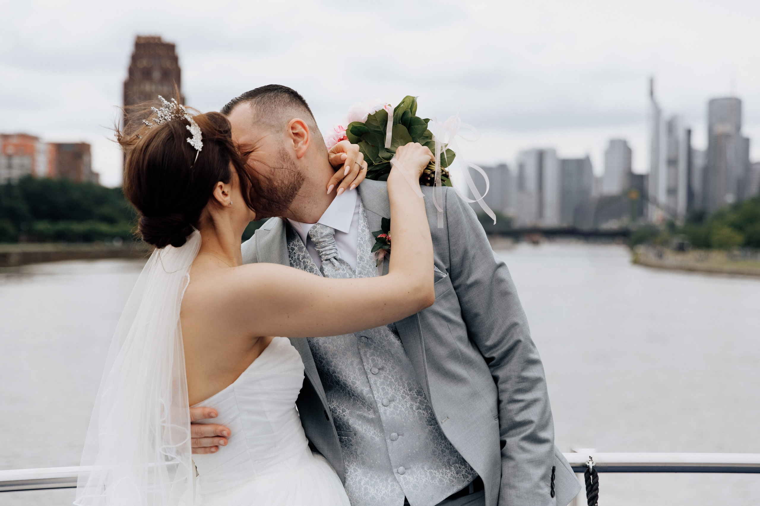 Der Bräutigam und die Braut küssen sich mit Blick auf Frankfurt und den Fluss Main. Ein romantischer und unvergesslicher Moment der Hochzeit.