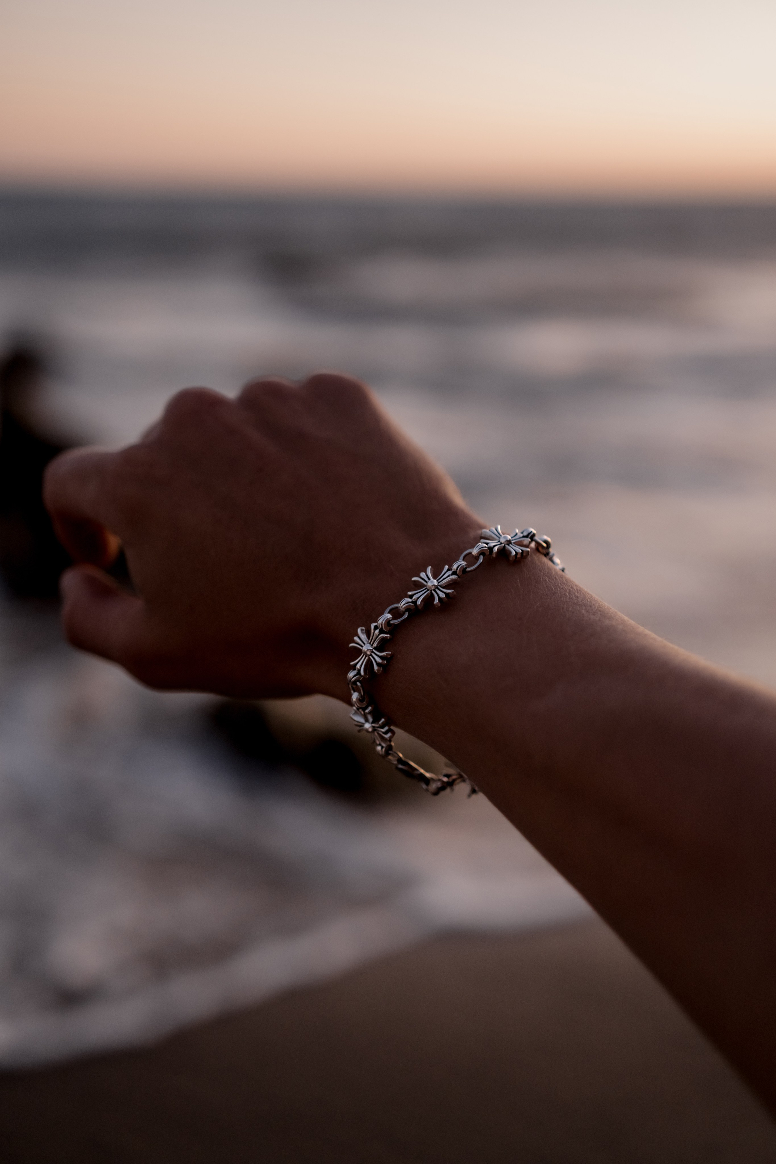 Detailed shot of a hand wearing a silver bracelet, gracefully reaching toward the ocean horizon.