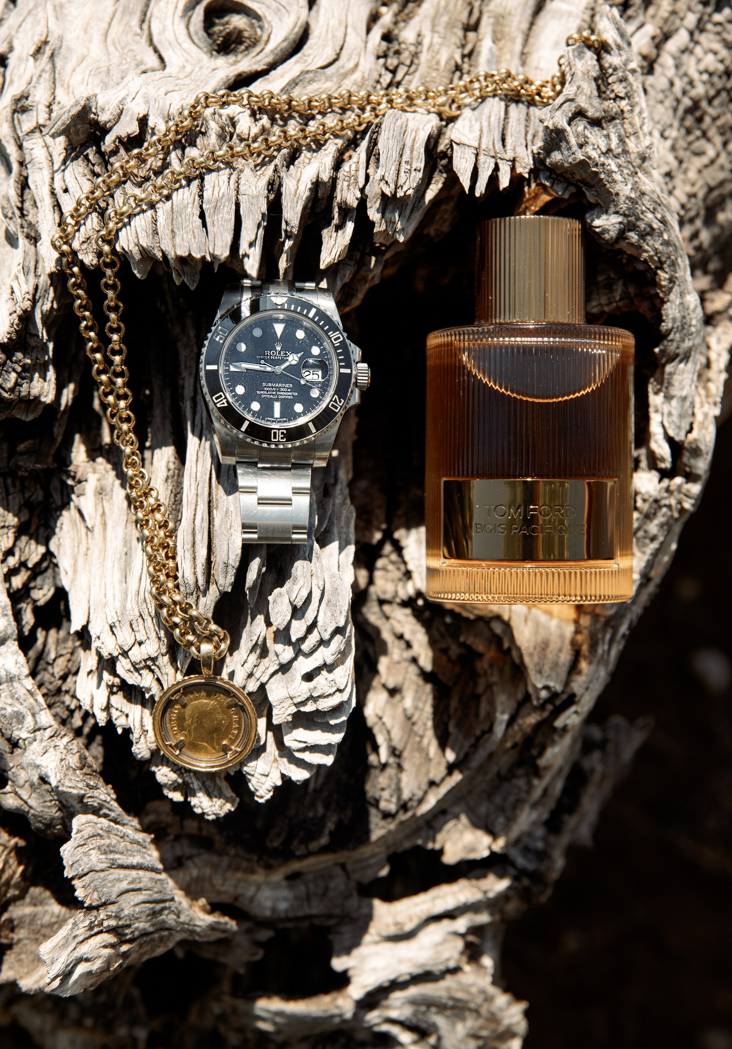 Luxury groom’s accessories: a vintage gold Rolex watch with a champagne dial, a thick polished gold chain, and an elegant glass bottle of woody amber perfume