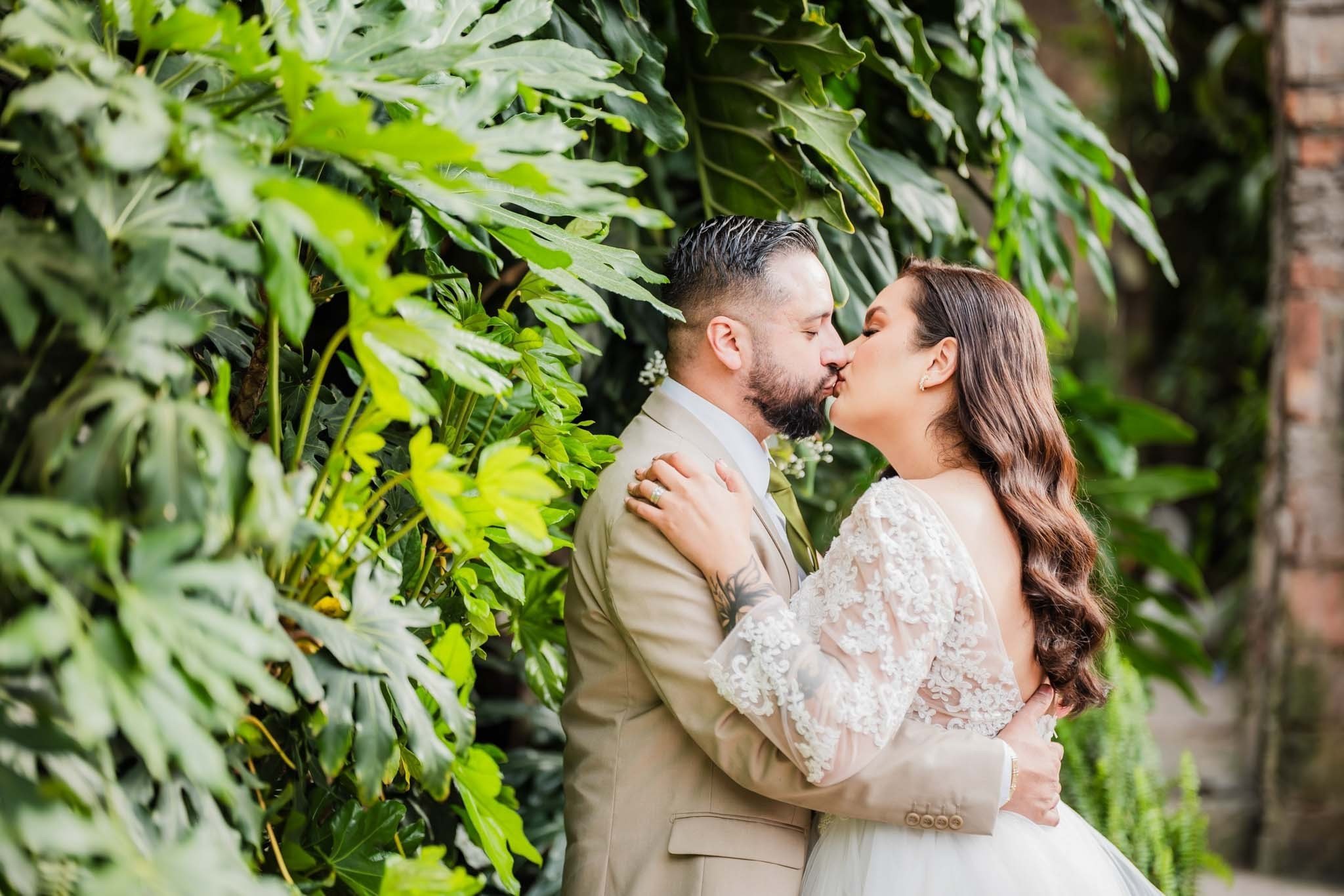 Fotografía de boda en Jardín Casa Baga Rosarito, pareja de novios besándose rodeados de vegetación, fotógrafo profesional de bodas en Tijuana Baja California, sesión romántica en jardín