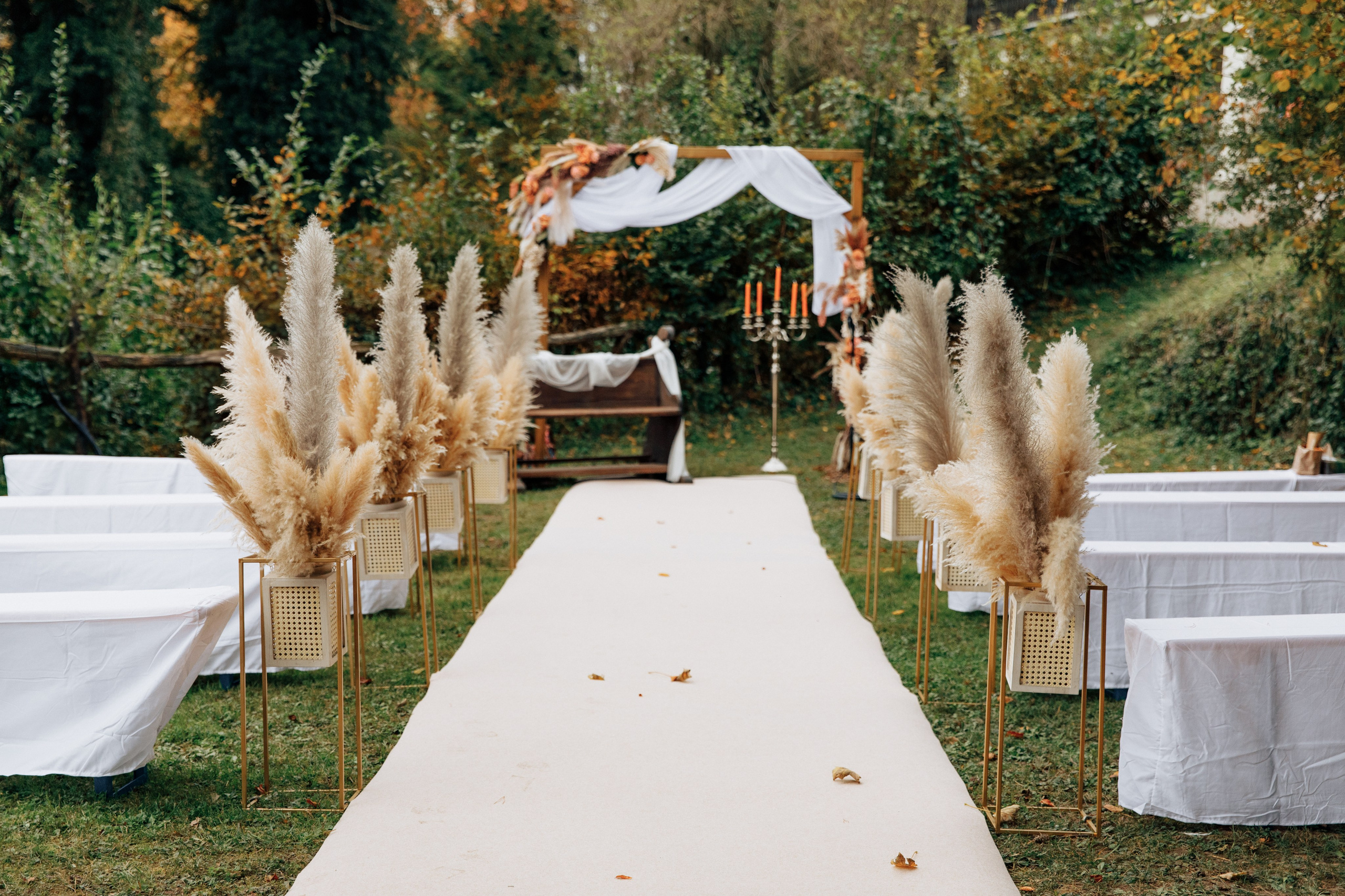 Ein weißer Gang führt zum Hochzeitsbogen, an den Seiten ist Pampasgras in herbstlichen Farbtönen. Alles ist in warmen, herbstlichen Farben gehalten.