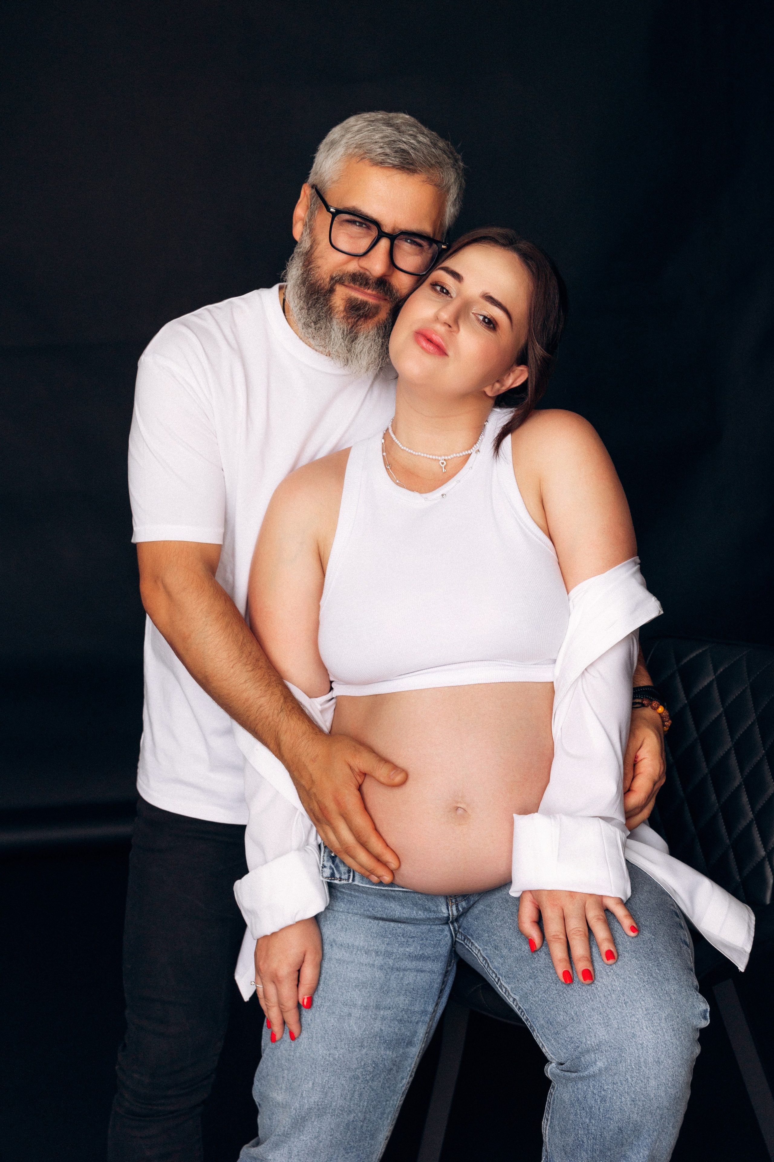 Intymna fotografia ciążowa – kobieta siedzi blisko partnera, ciepły kontakt wzrokowy, bliskość i zaufanie.