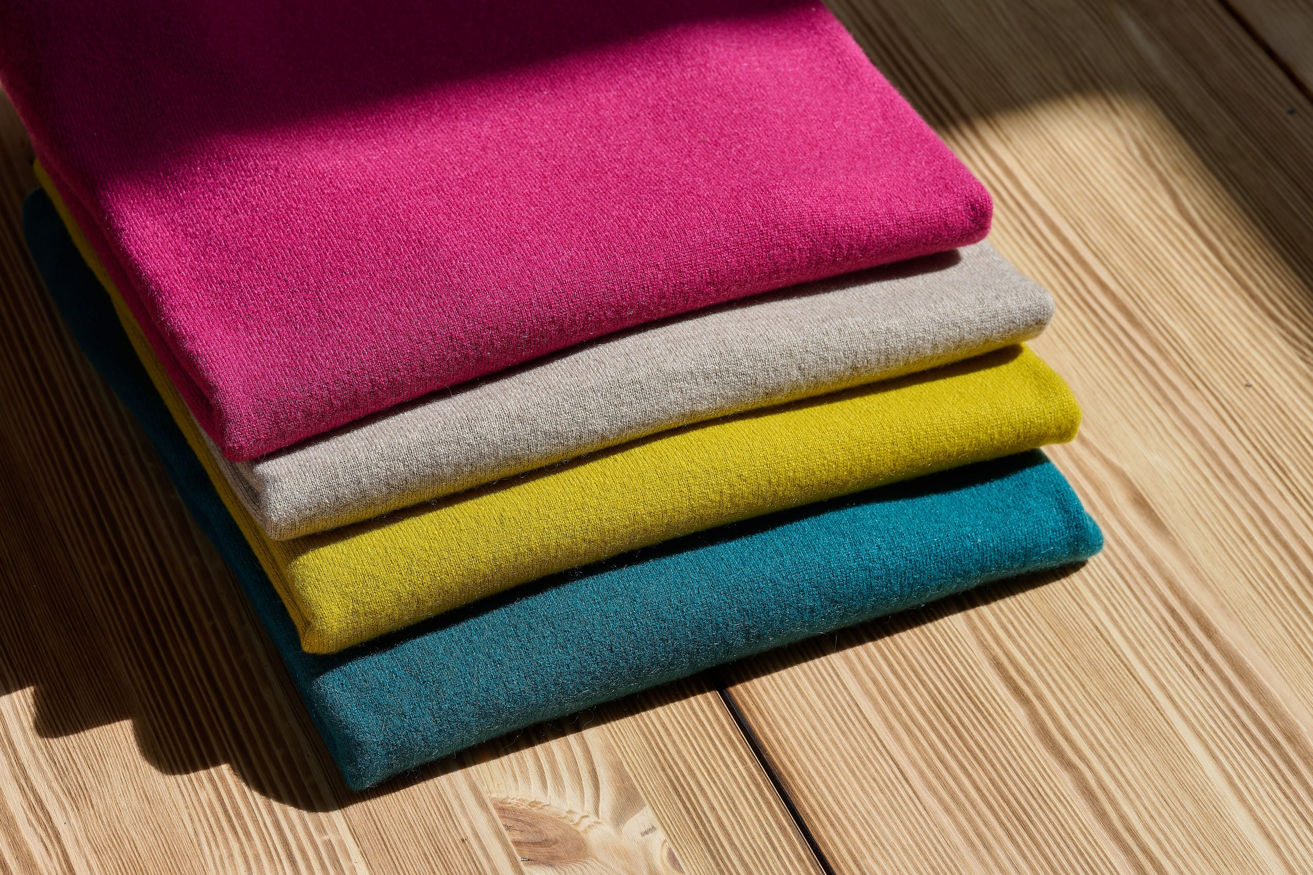 Produktfotografie Wien – Stapel farbiger Stoffe in Pink, Grün, Blau und Gelb auf Holztisch.