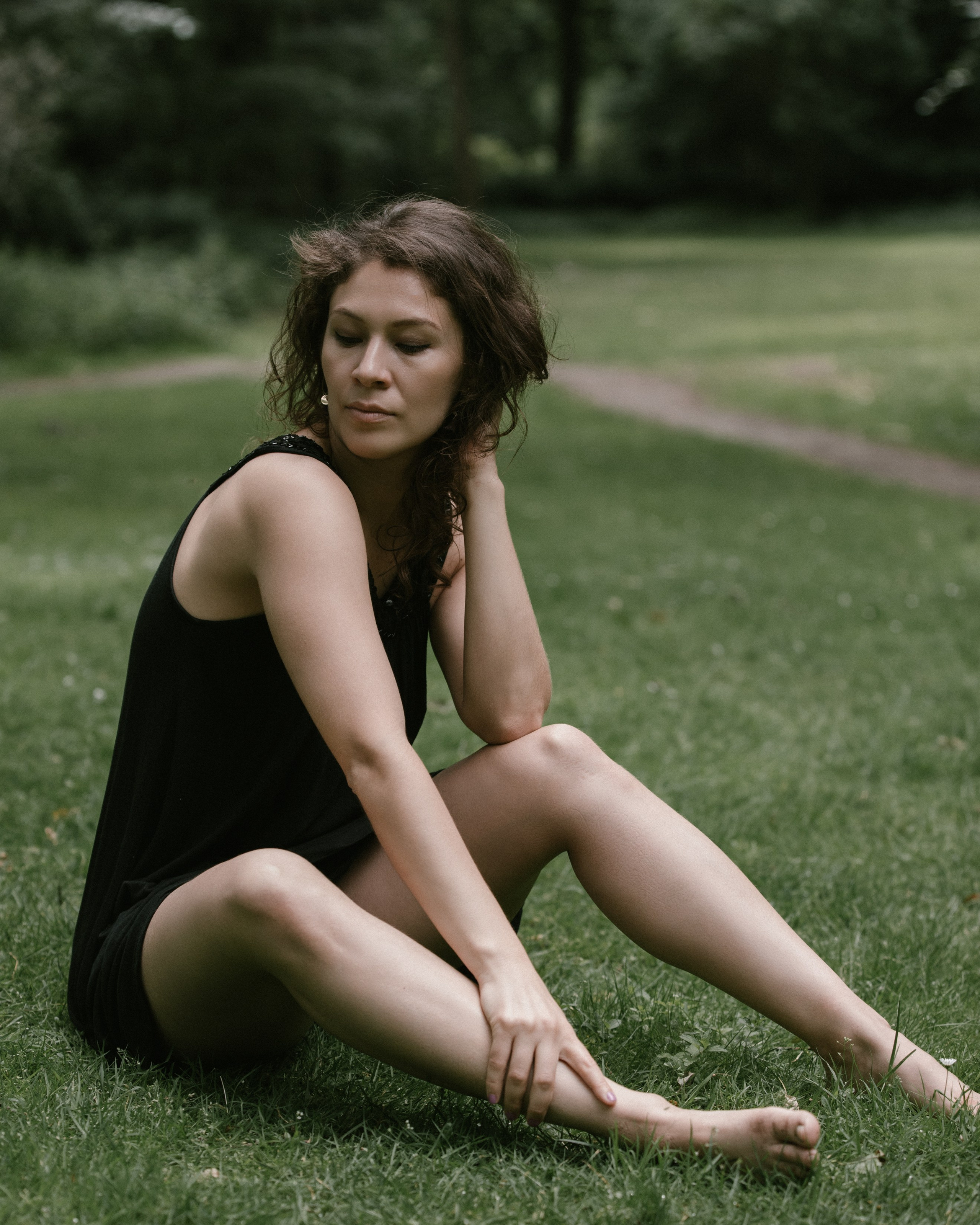 Tänzerin auf Gras sitzend, Hand am Bein ruhend