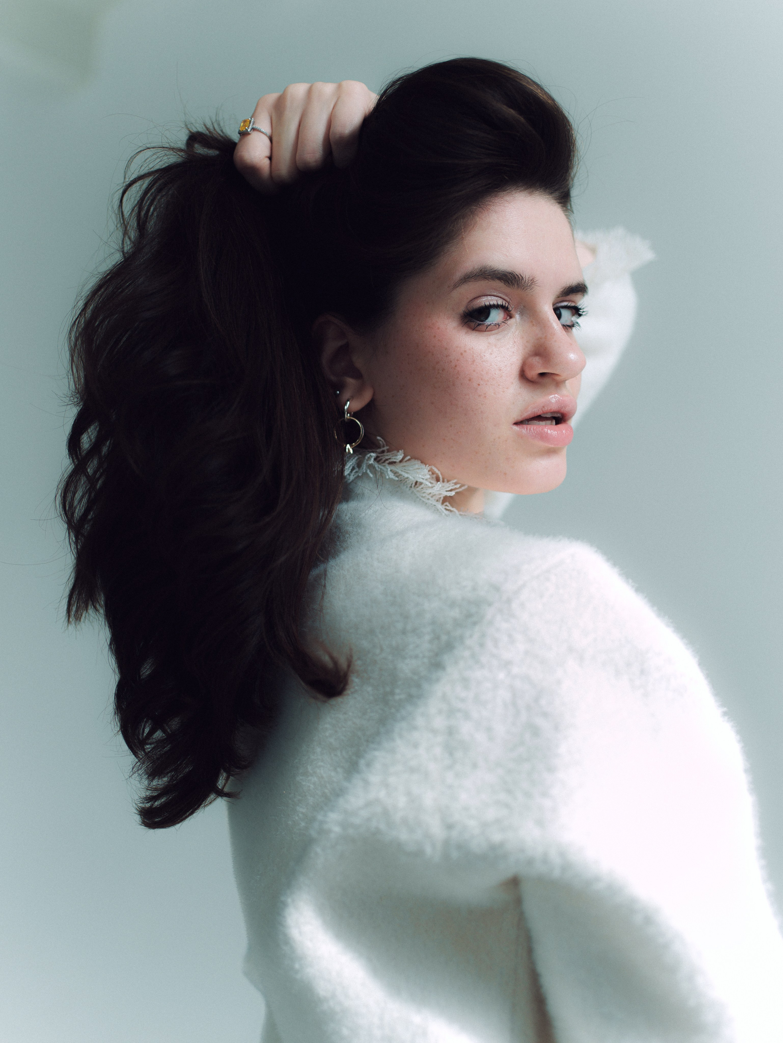 Relaxed pose in white cardigan, minimal studio atmosphere