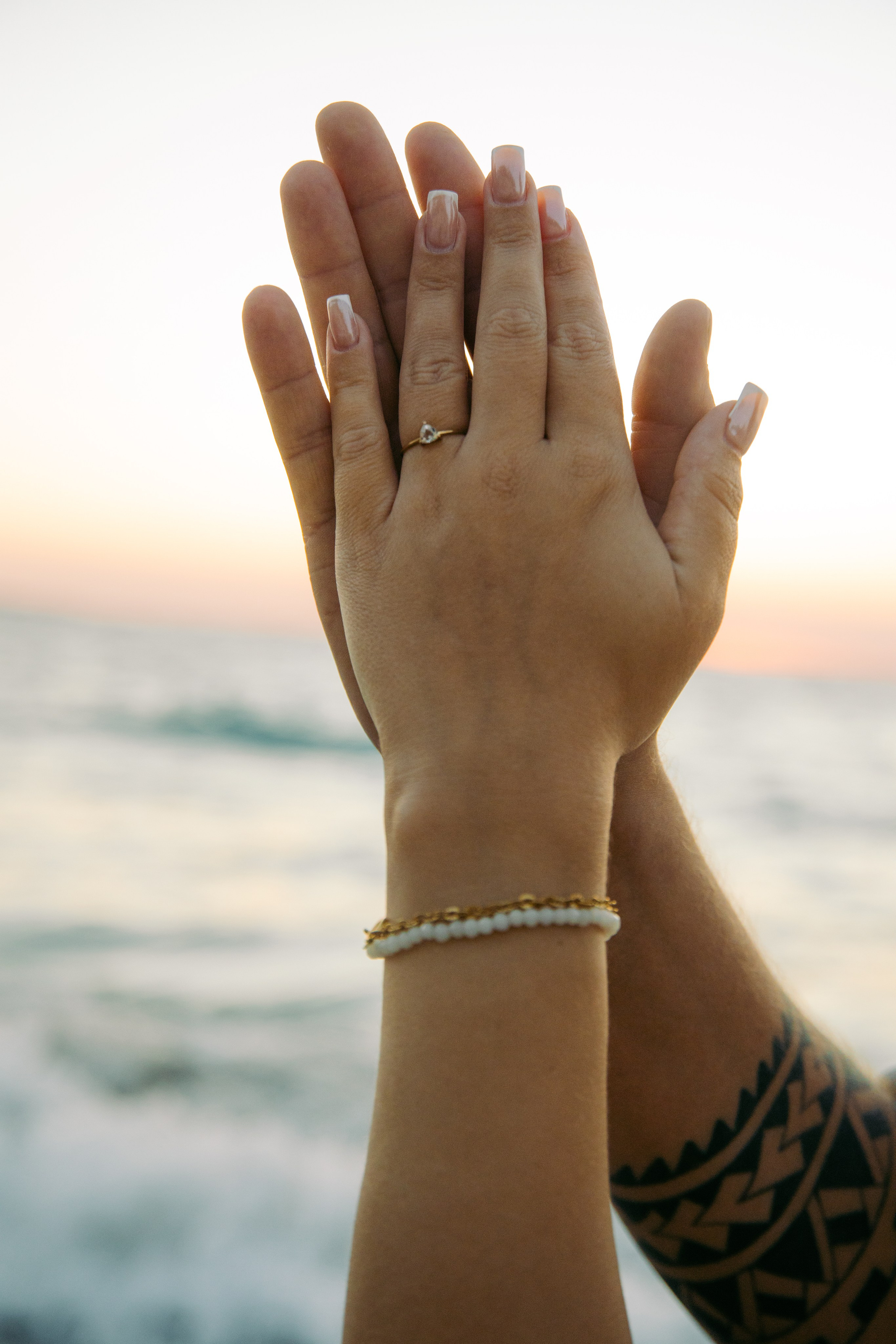 "Hand in Hand am Kato Petres: Detailaufnahme zweier sich haltender Hände über dem steinigen Ufer. Ein Symbol der Zweisamkeit vor der wilden, natürlichen Schönheit der Westküste von Rhodos."