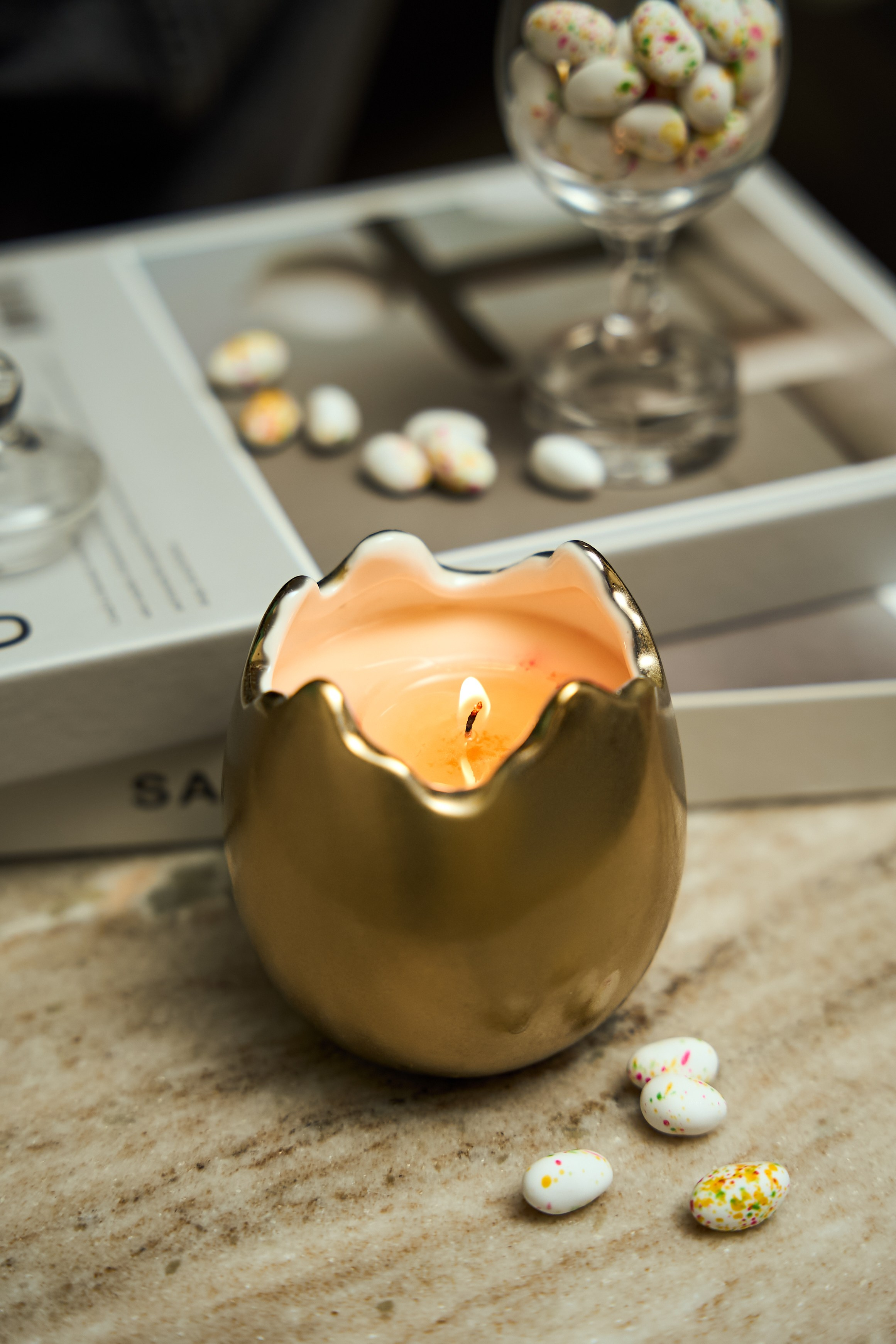 Lit decorative candle with warm glow beside candies and a glass bowl
