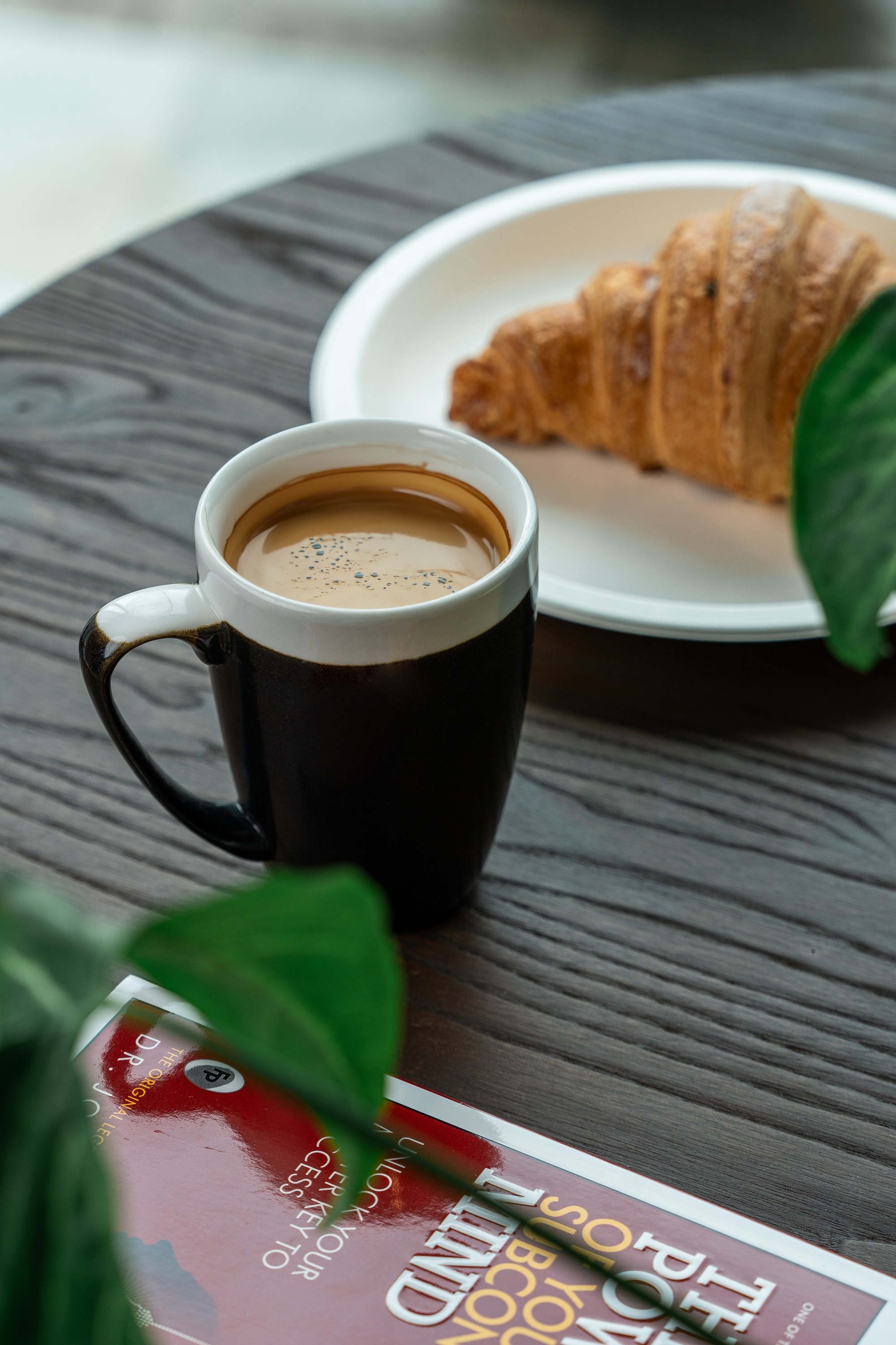 Qara fincanda qəhvə, kruvasan və masa üzərində "The Power of Your Subconscious Mind" kitabı.