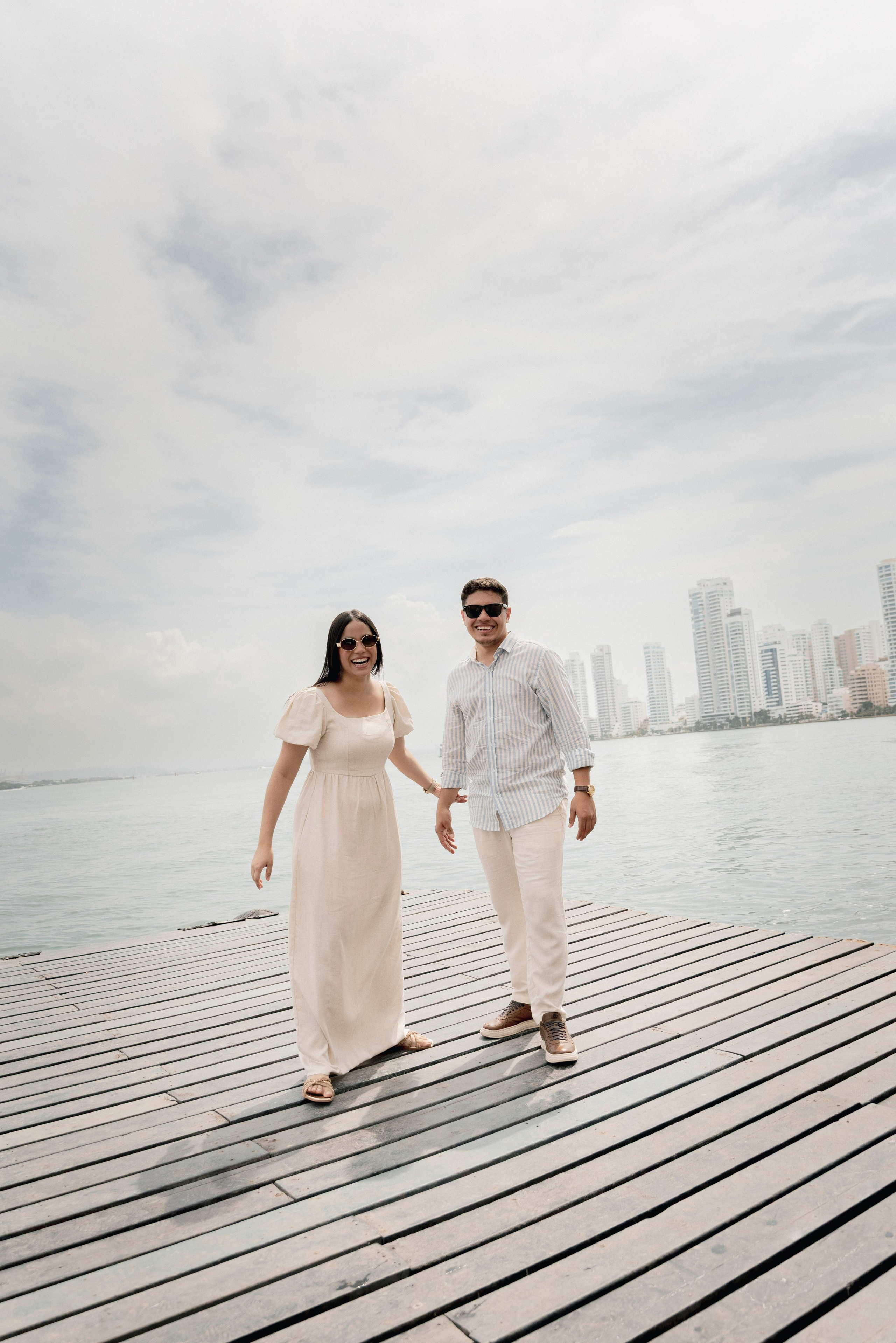 Novios caminando por pasarela de madera, sesión cinematográfica de pareja en Cartagena
