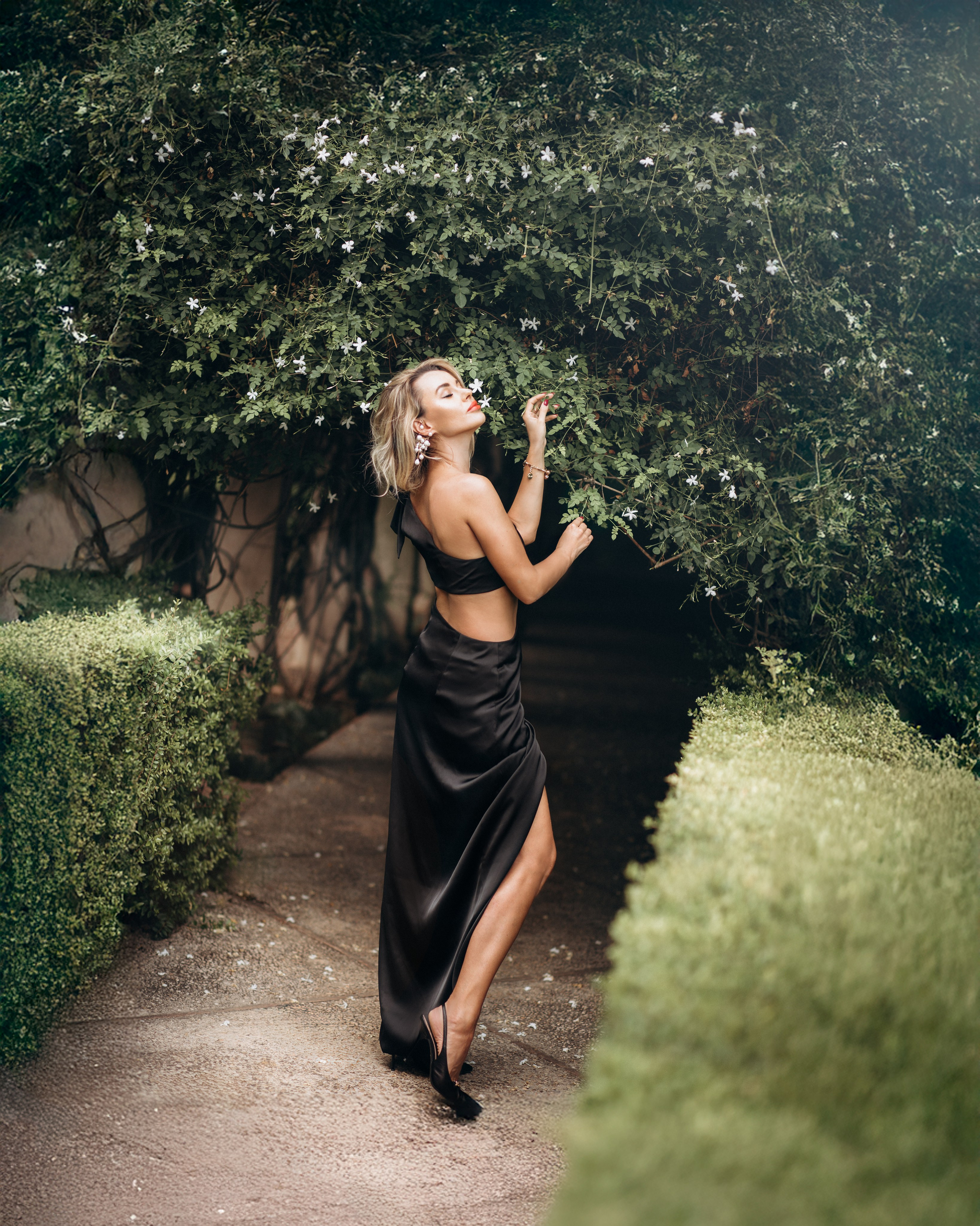 Стильная портретная съёмка в Сан-Себастьяне, Испания — элегантная женщина в чёрном платье позирует на фоне зелёного сада, передавая красоту и утончённость. Подходит для тех, кто ищет модную и художественную портретную съёмку в Сан-Себастьяне и на севере Испании.