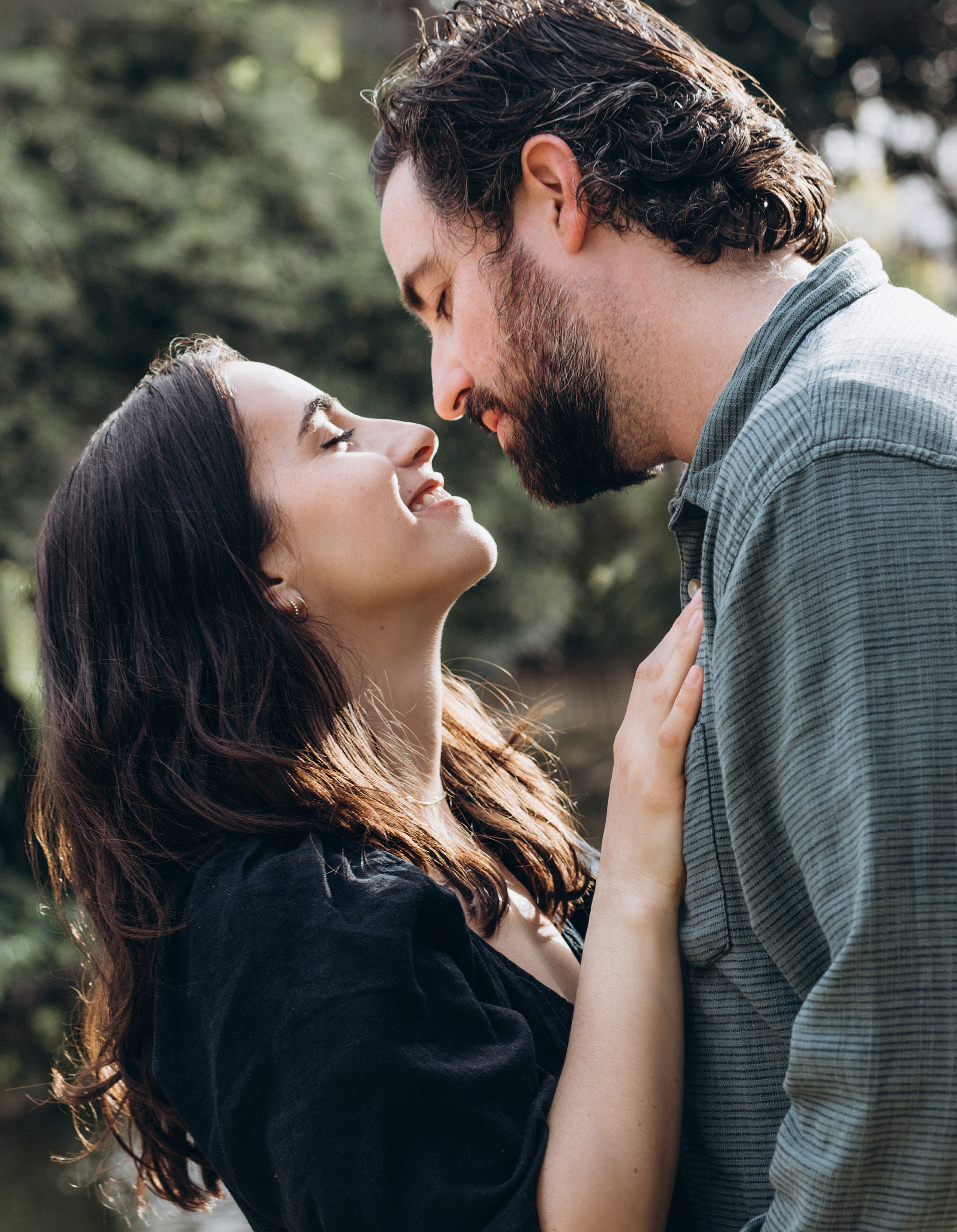 Tender moment between a couple gazing into each other’s eyes, about to kiss, surrounded by nature and soft sunlight — a romantic love story portrait capturing intimacy and connection.