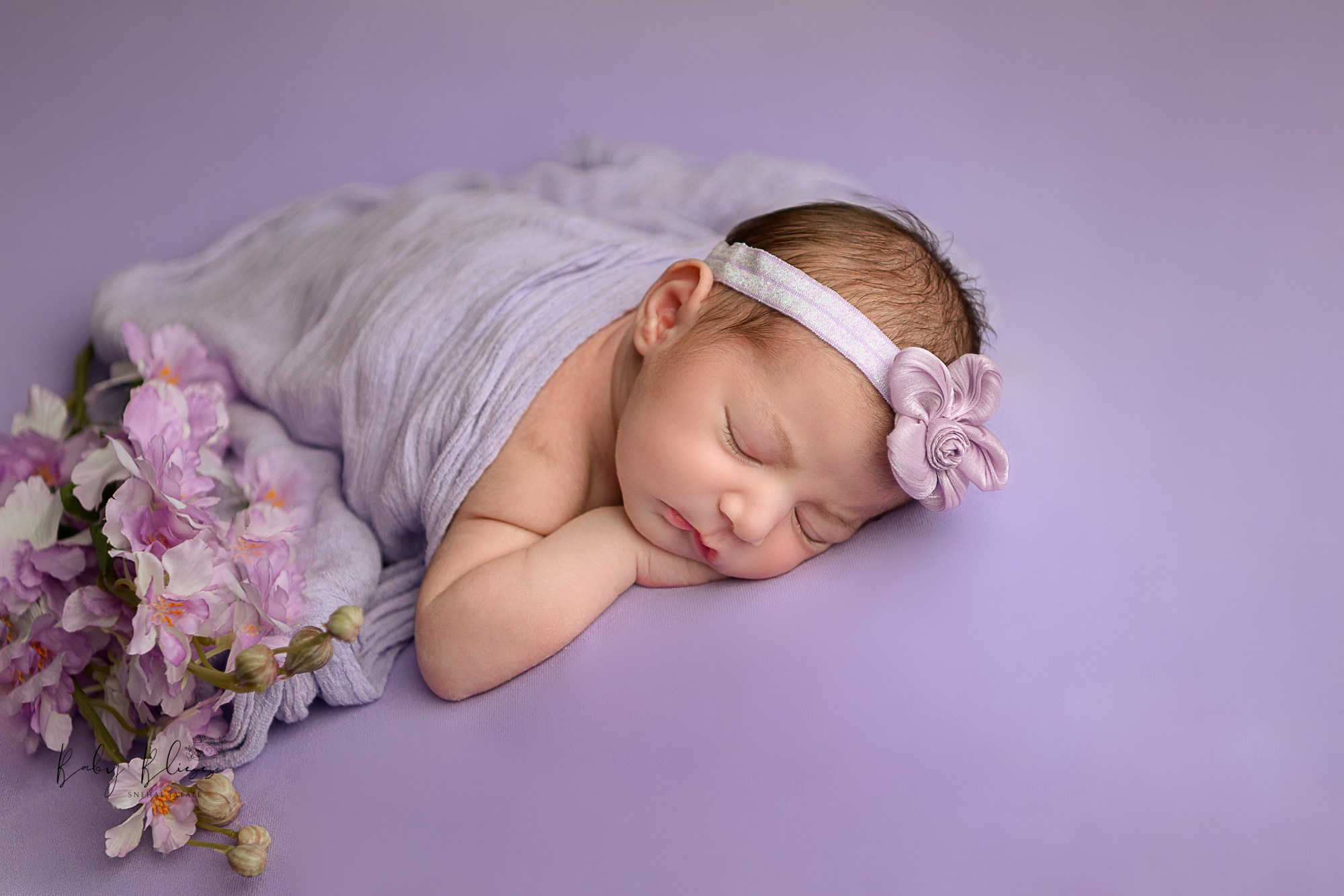 peacefully sleeping newborn baby girl with lavender floral arrangements beside her.
