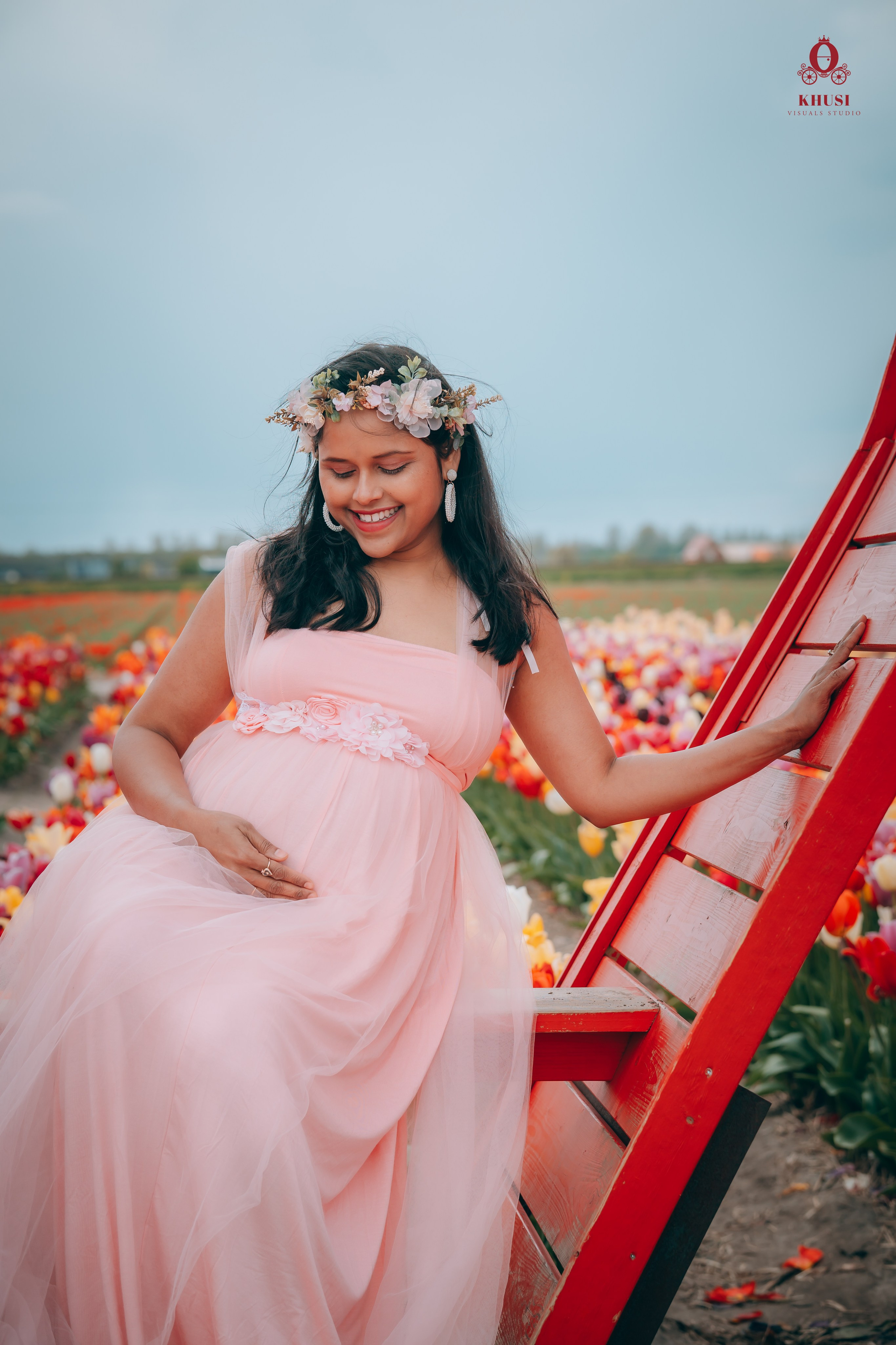 A pregnant woman sitting on a red structure in a tulip field in netherlands