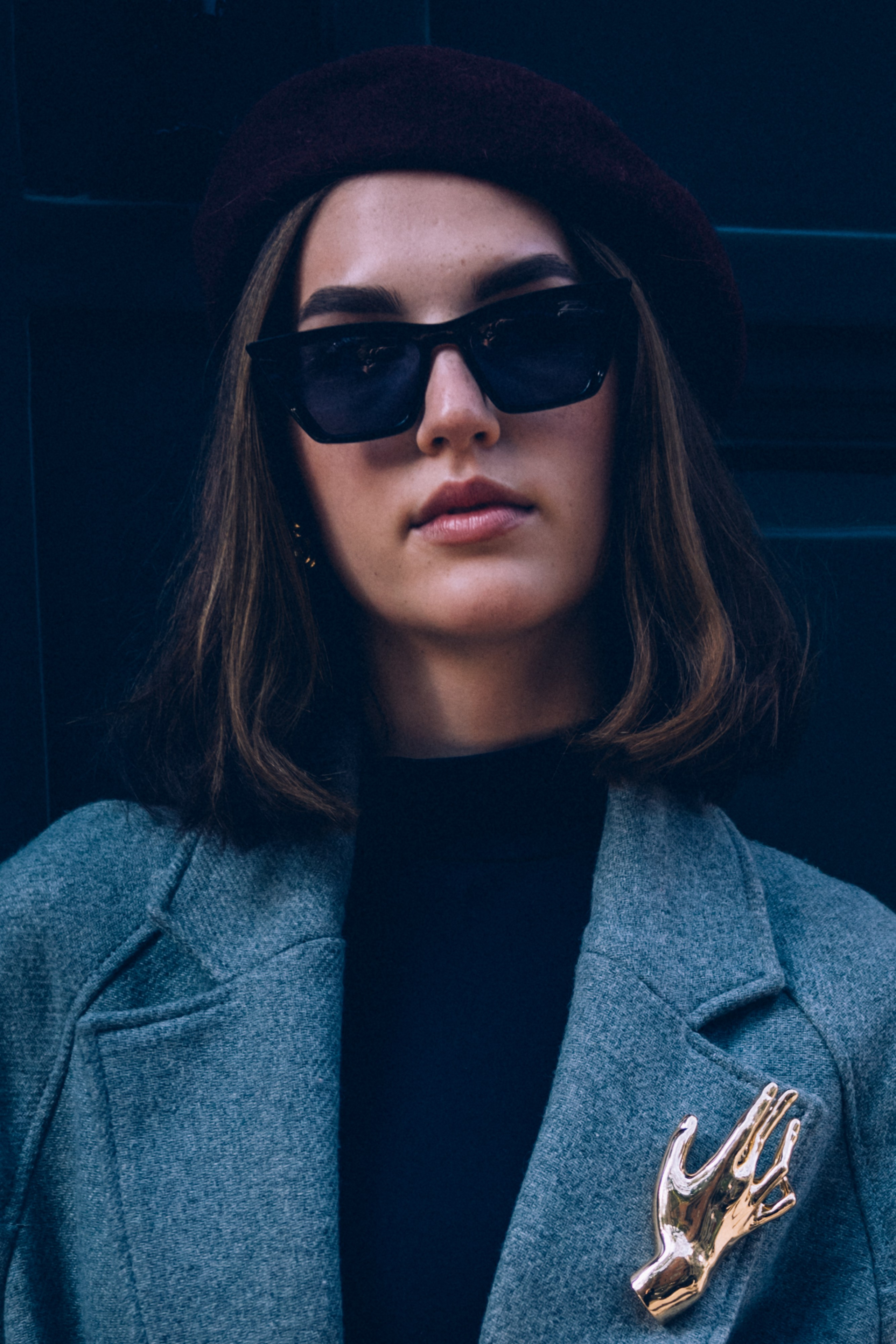 Stylish close-up of a woman wearing a burgundy beret, oversized sunglasses, and a gray coat adorned with a striking gold brooch, exuding modern french elegance in Milan