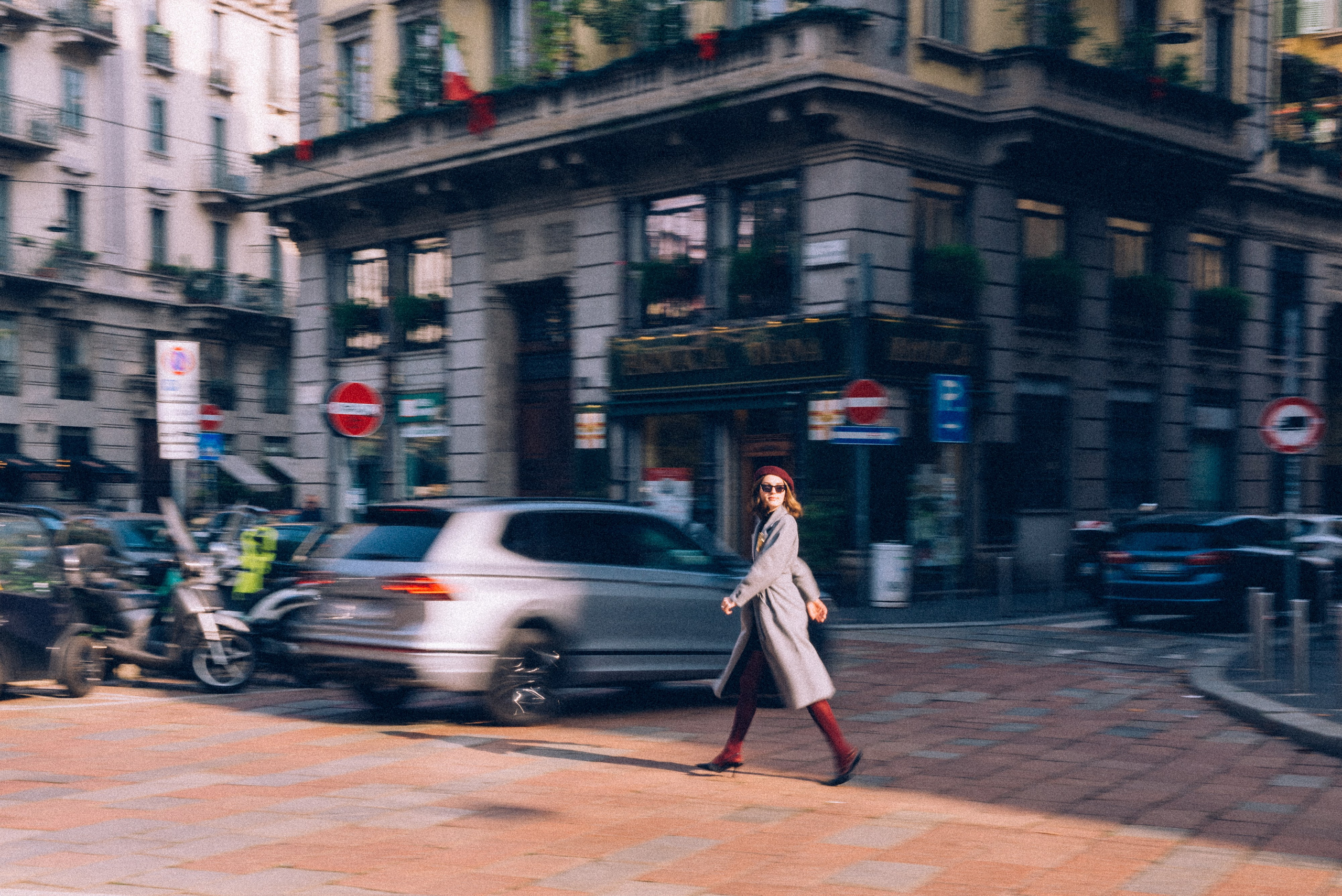 Dynamic shot of a stylish woman walking through Milan's bustling streets, wearing a gray coat and chic accessories, capturing the city's vibrant energy