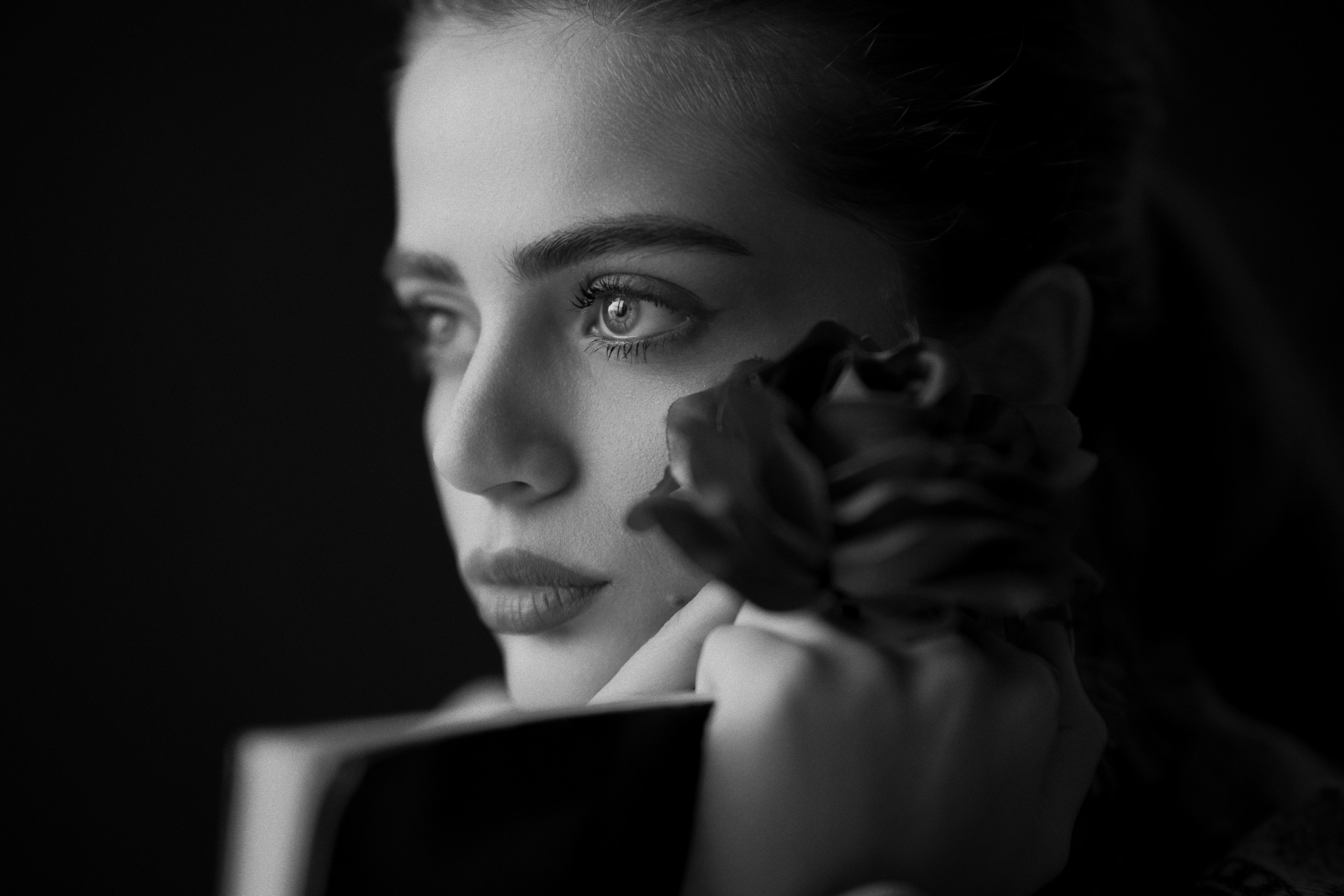 Black and white female portrait photography by Mehran Hadad featuring a young woman holding a flower with soft fine art lighting.