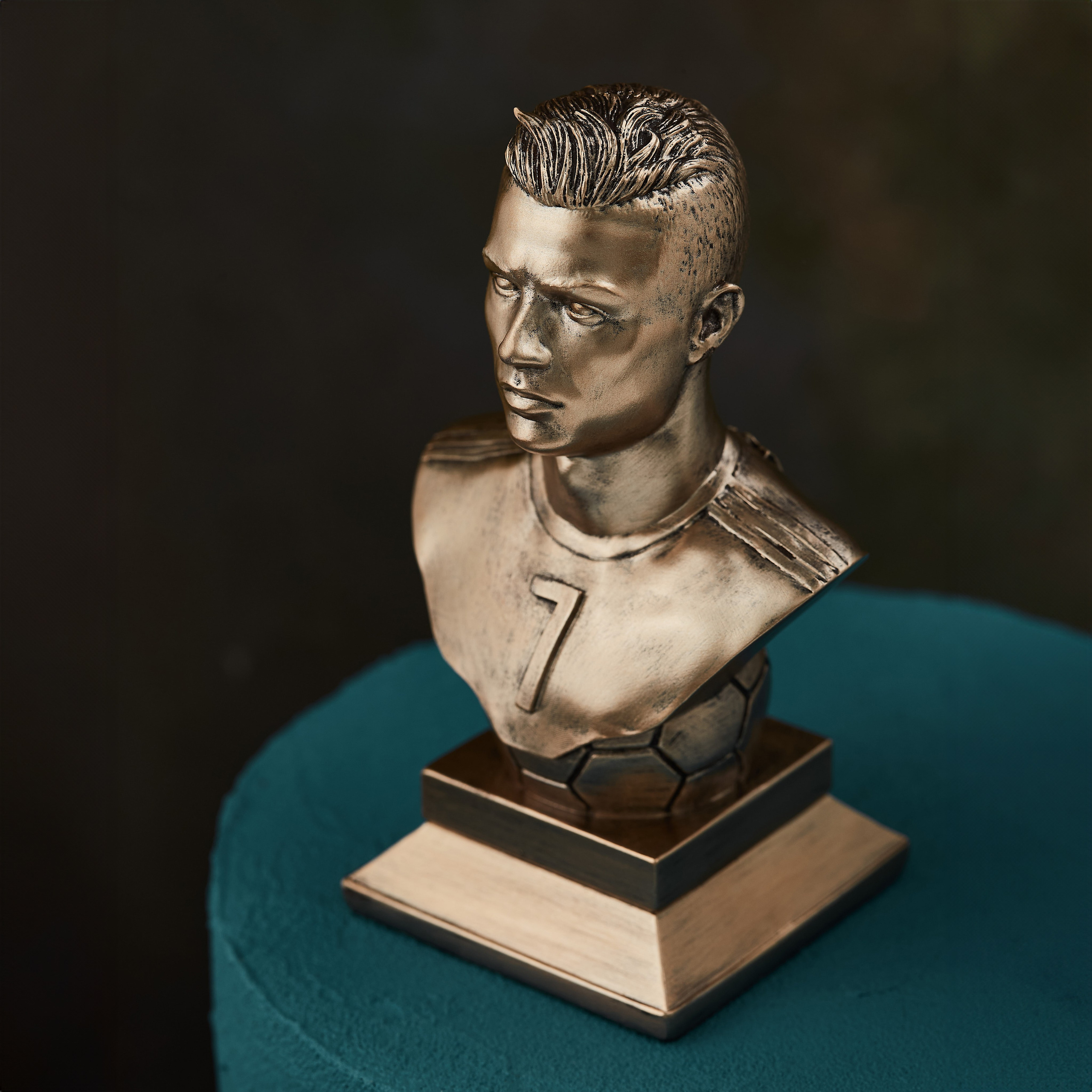 Kriştiano Ronaldonun bürünc büstü, 7 nömrəli forması ilə, tünd mavi fonda firuzəyi parça üzərində dekorativ obyekt.