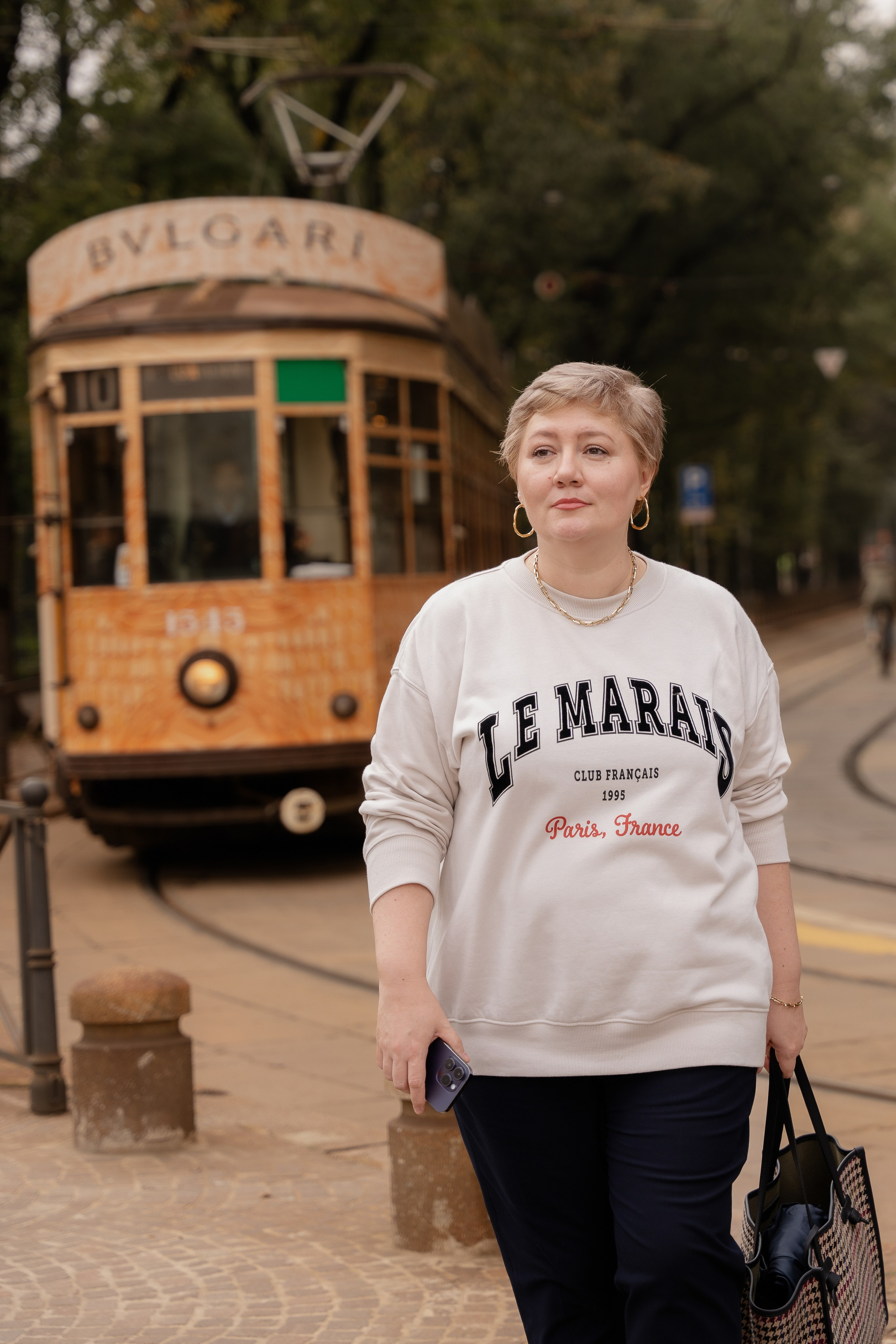 На первом плане девушка в светлой толстовке, на заднем плане трамвай в Милане