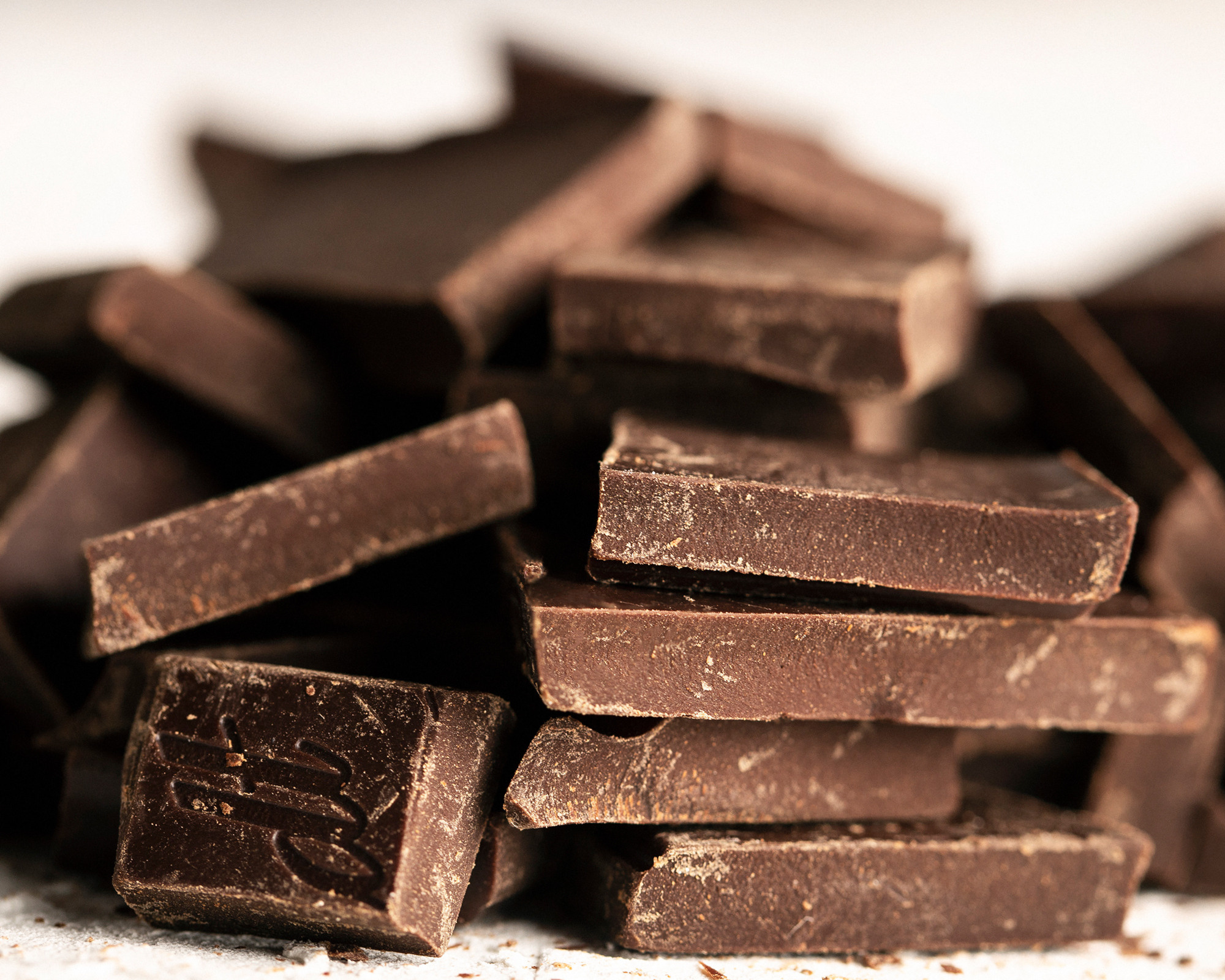 Chunks of rich dark chocolate stacked on a neutral surface for dramatic contrast