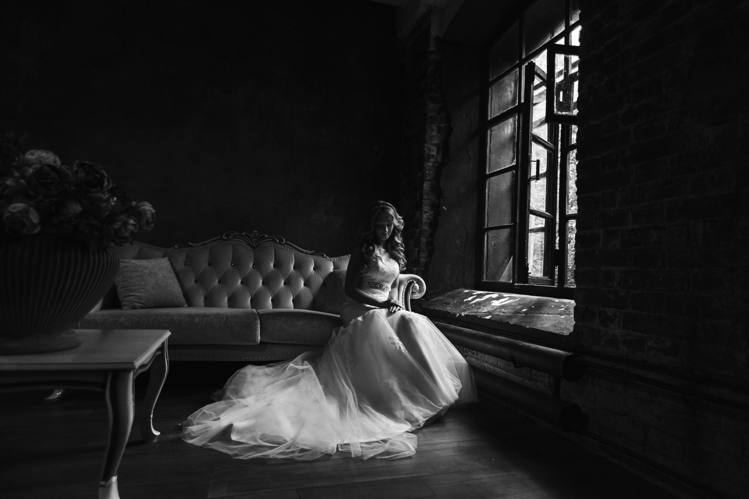 Braut sitzt auf einem schönen Sofa in einem alten Zimmer bei Fensterlicht.