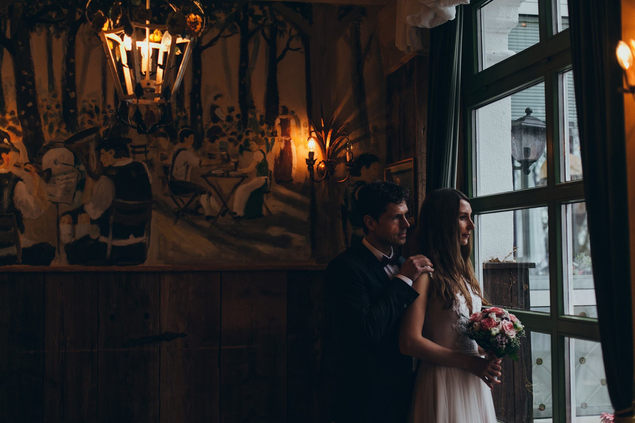 Das Brautpaar steht in einem eleganten Restaurant am Tegernsee und schaut aus dem Fenster.