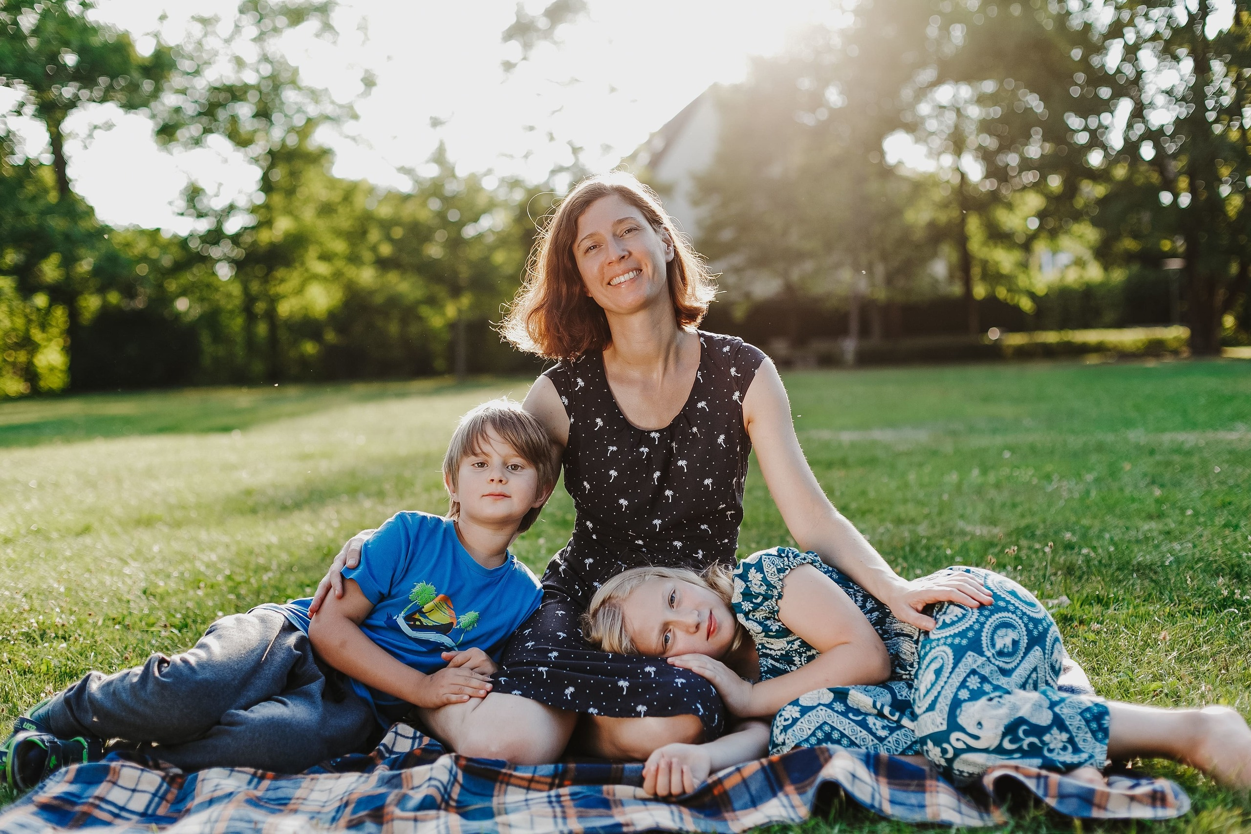 Alleinerziehende Mutter sitzt mit Tochter und Sohn auf einer Wiese.