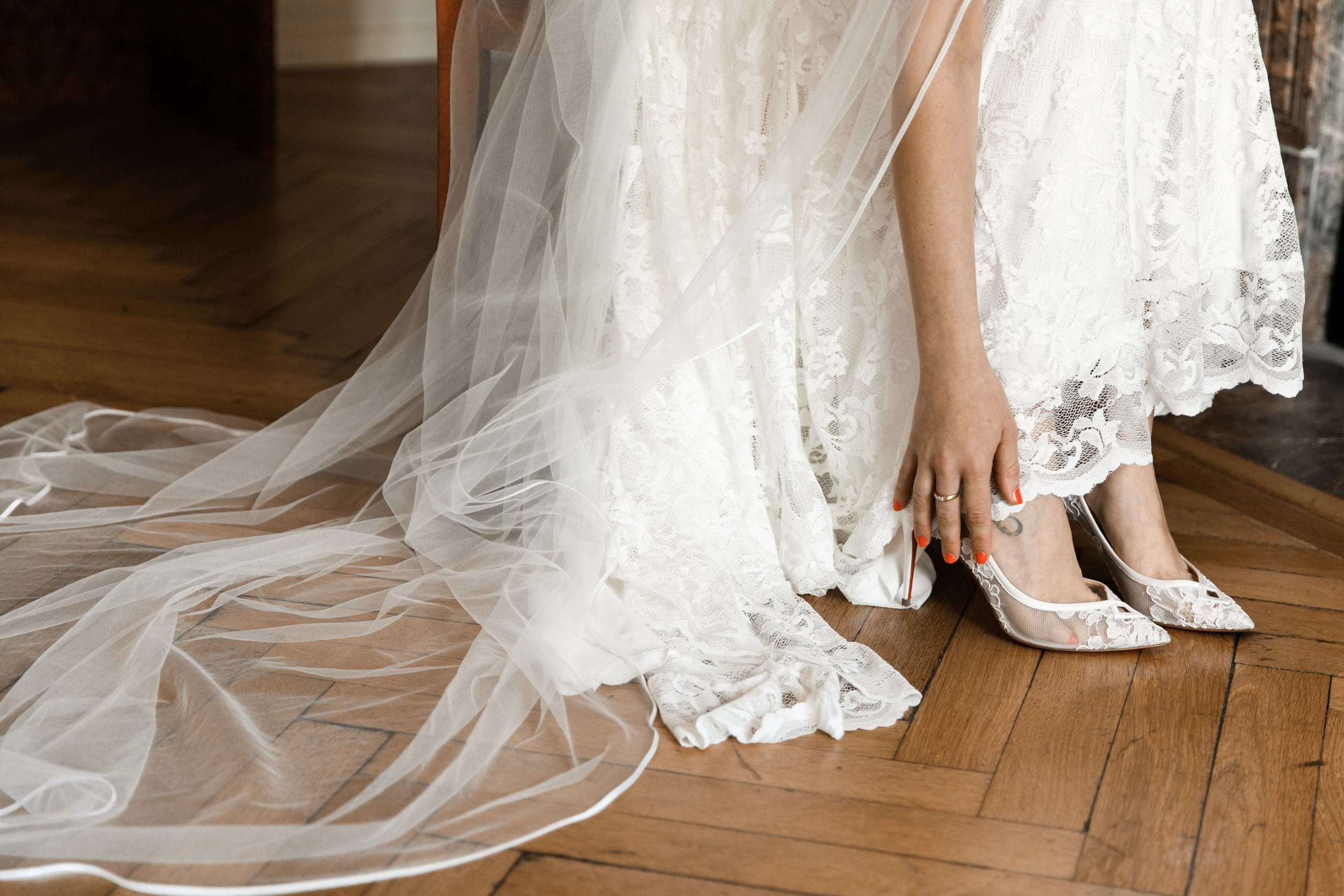 Details des Brautkleides, Schleier und die Hand der Braut, die ihre Schuhe zurechtrückt.