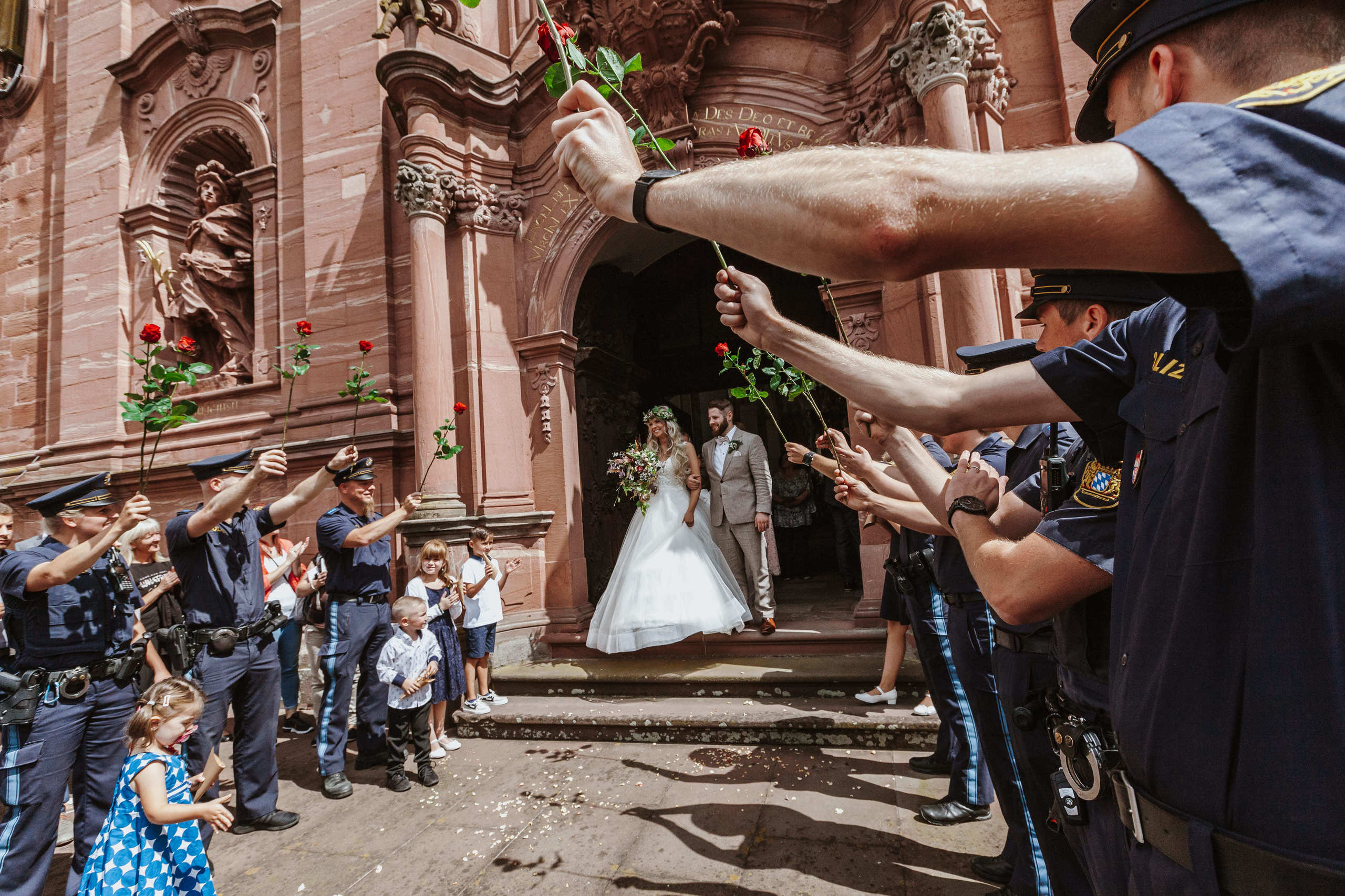 Braut und Bräutigam verlassen die Kirche und werden von einem Spalier aus Polizisten mit Rosen begrüßt.