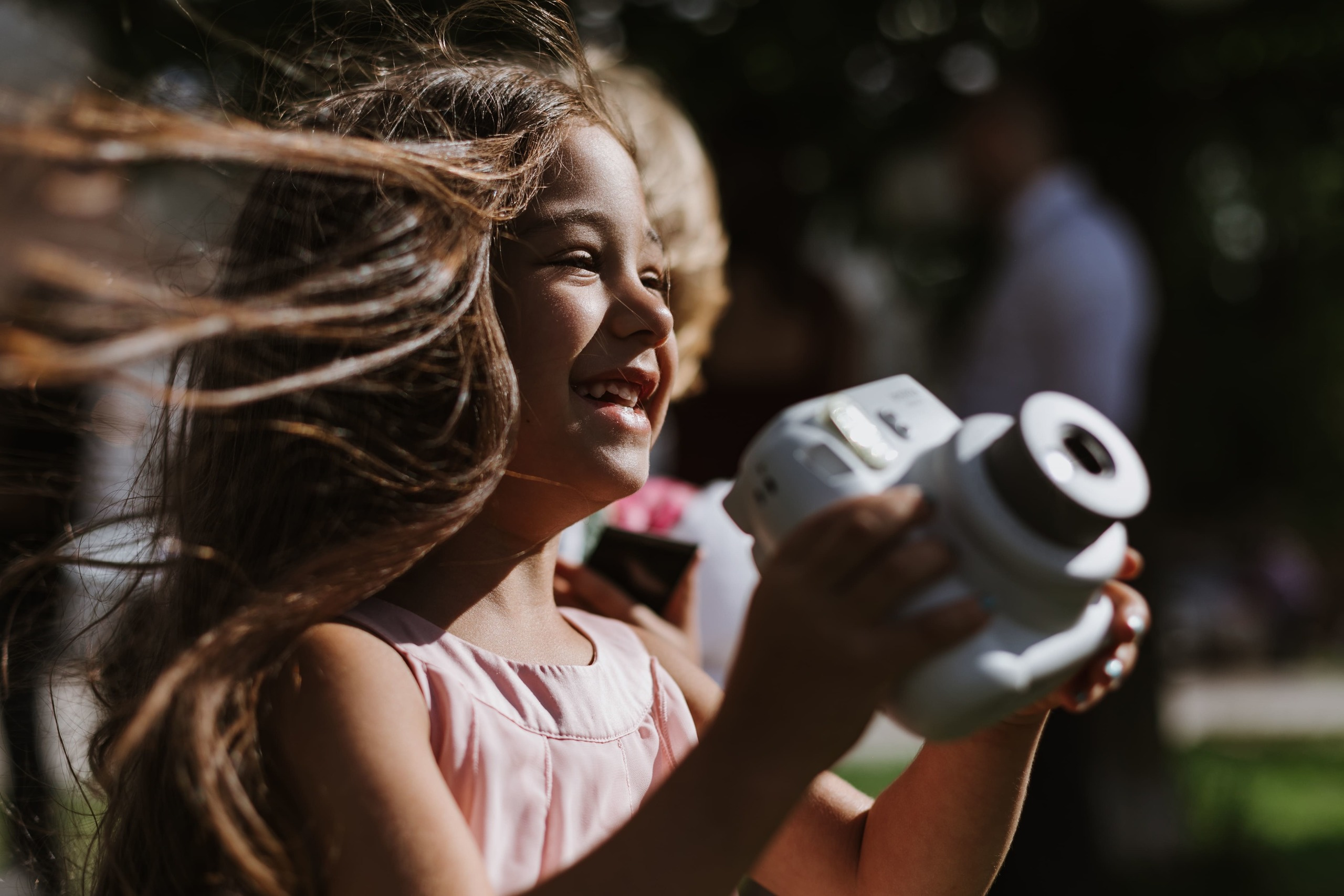 Mädchen hält eine Polaroid-Kamera in den Händen und lacht.
