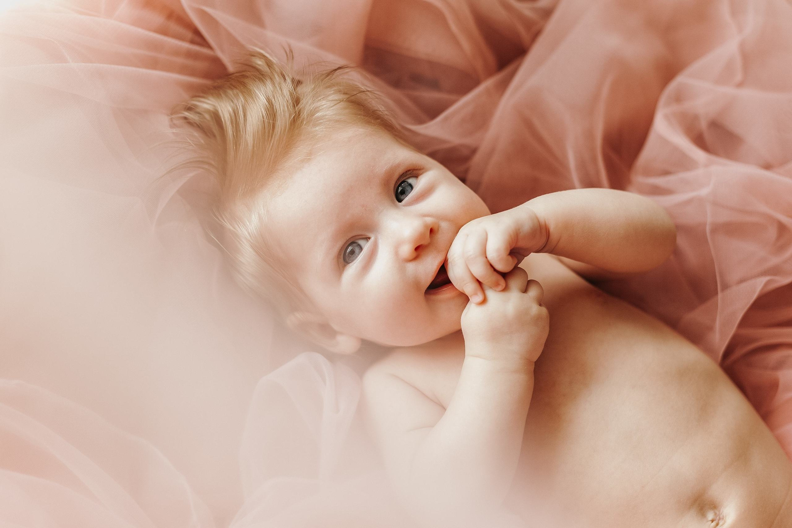 Baby liegt auf rosa Stoff und lächelt.