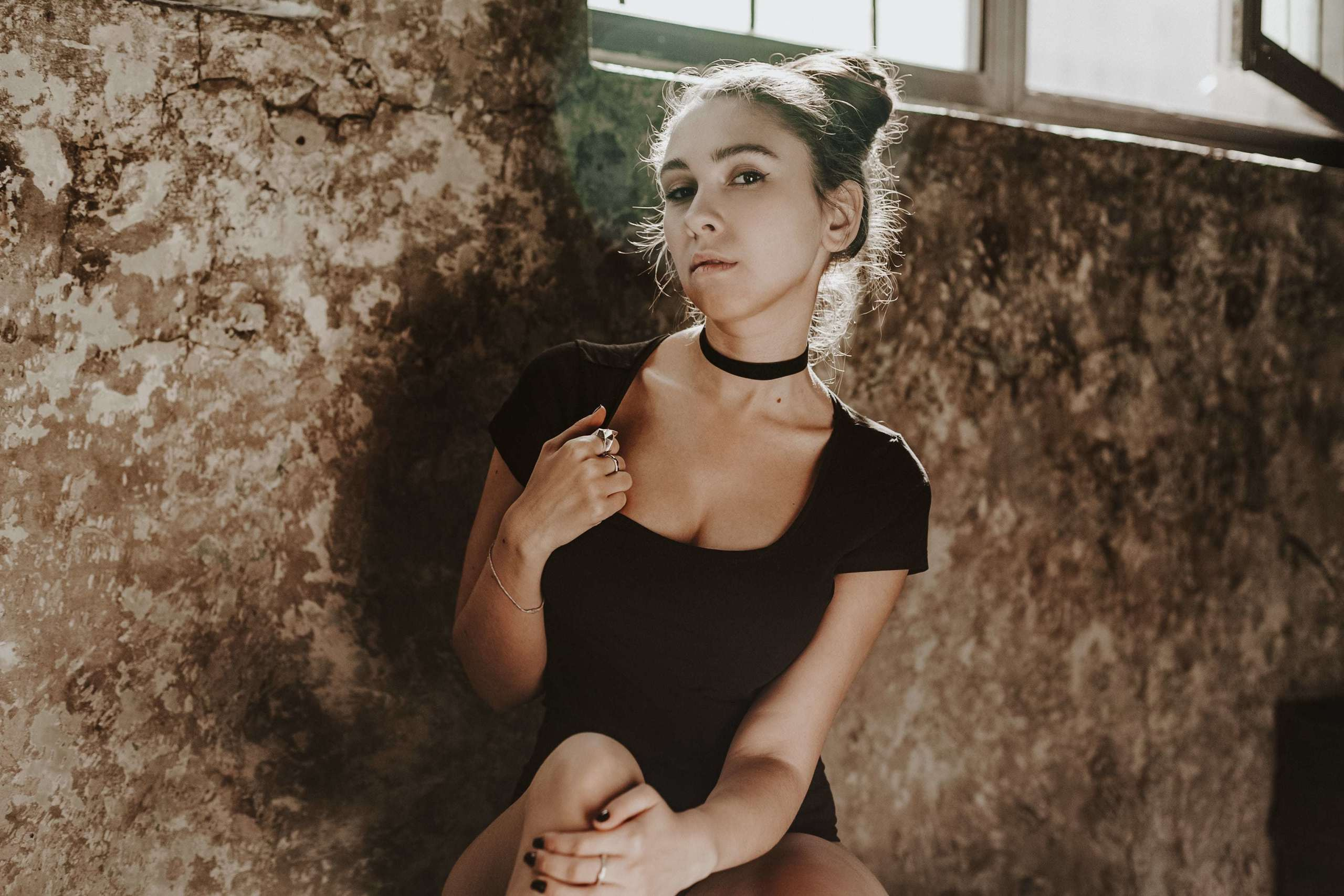 Frau blickt ruhig in die Kamera, durch das Fenster fällt warmes Licht auf ihr Gesicht.