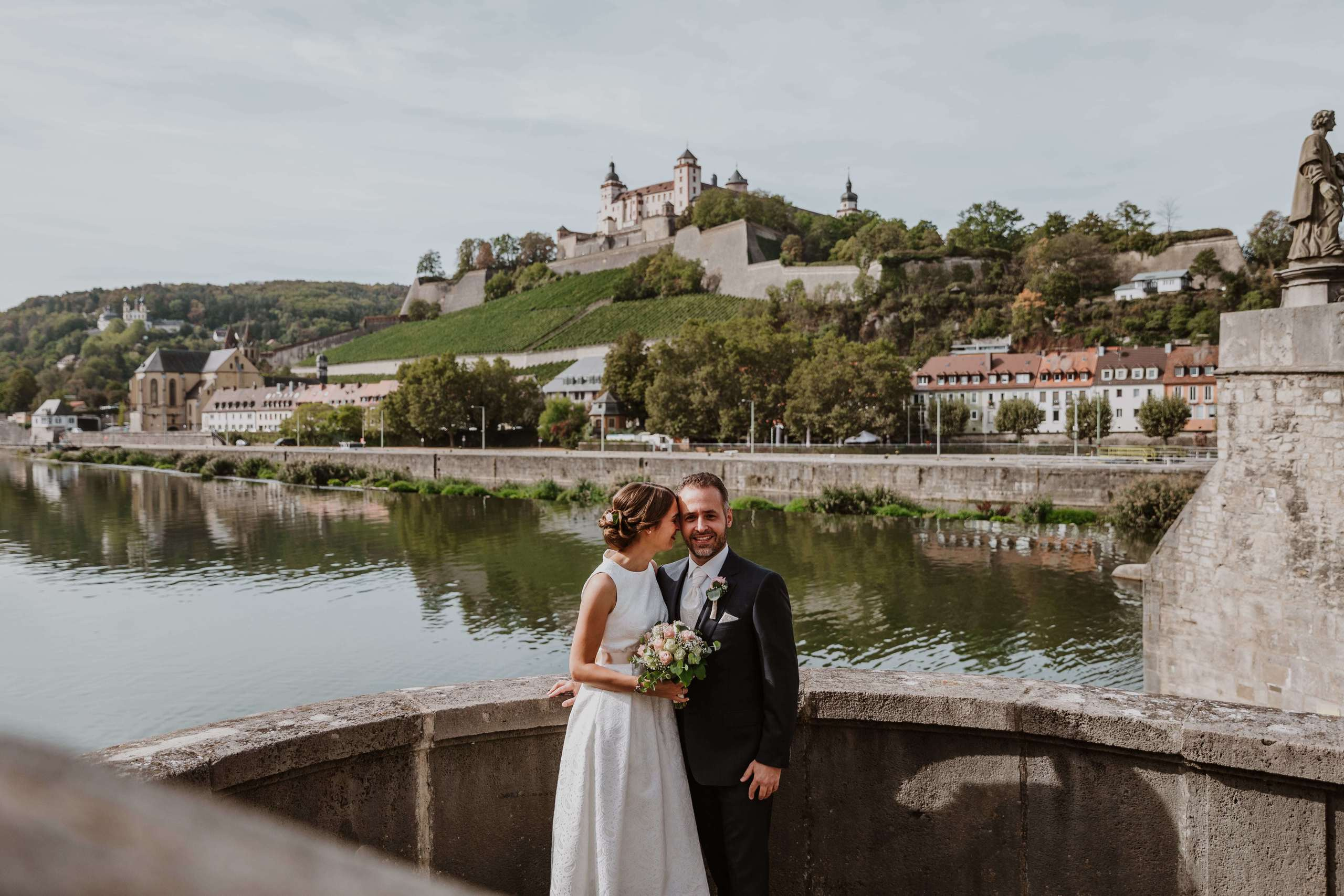 Bräutigam und Braut stehen auf der alten Mainbrücke in Würzburg.