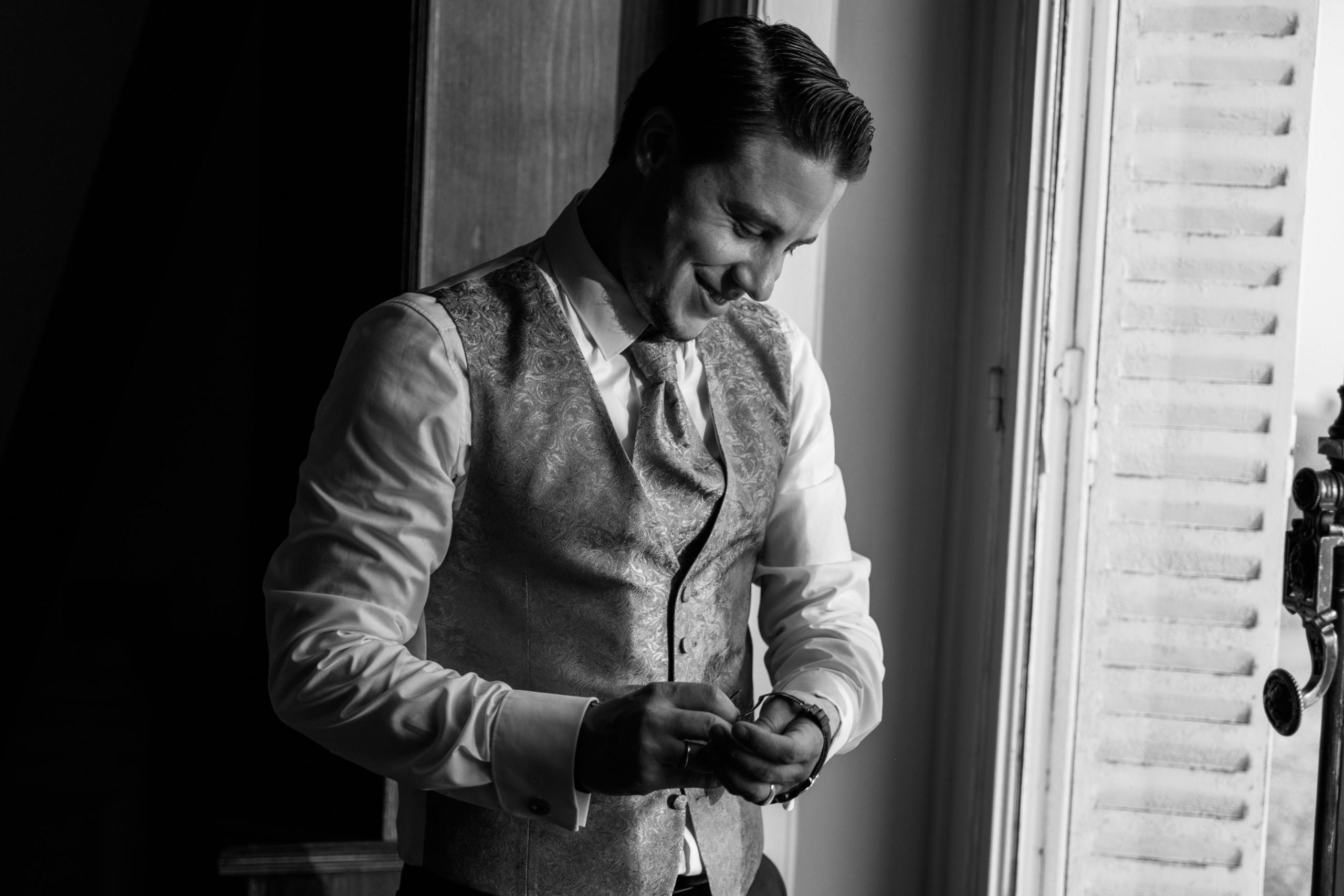 Der Bräutigam steht am Fenster und richtet seine Manschettenknöpfe.