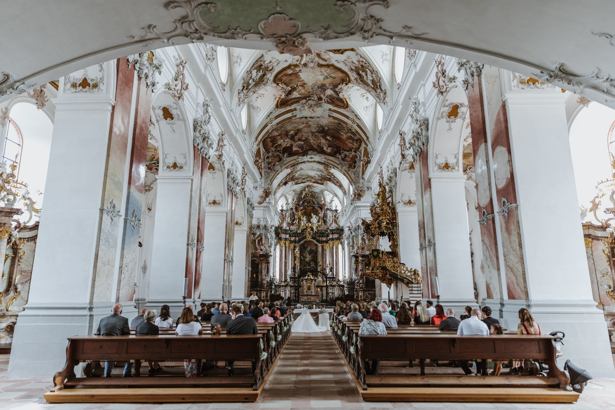 Panorama einer prächtigen Kirche, im Hintergrund sind die Rücken der Gäste und des Brautpaares zu sehen.