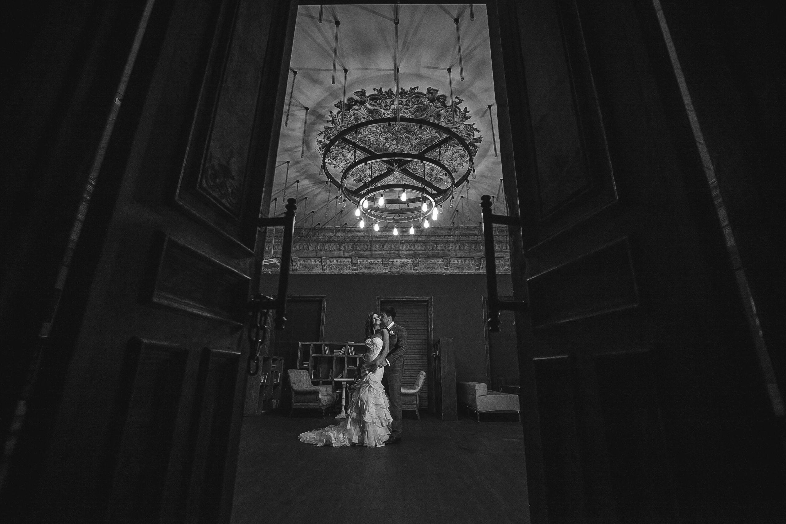 Bräutigam und Braut umarmen sich im historischen Saal unter einem schönen Kronleuchter.