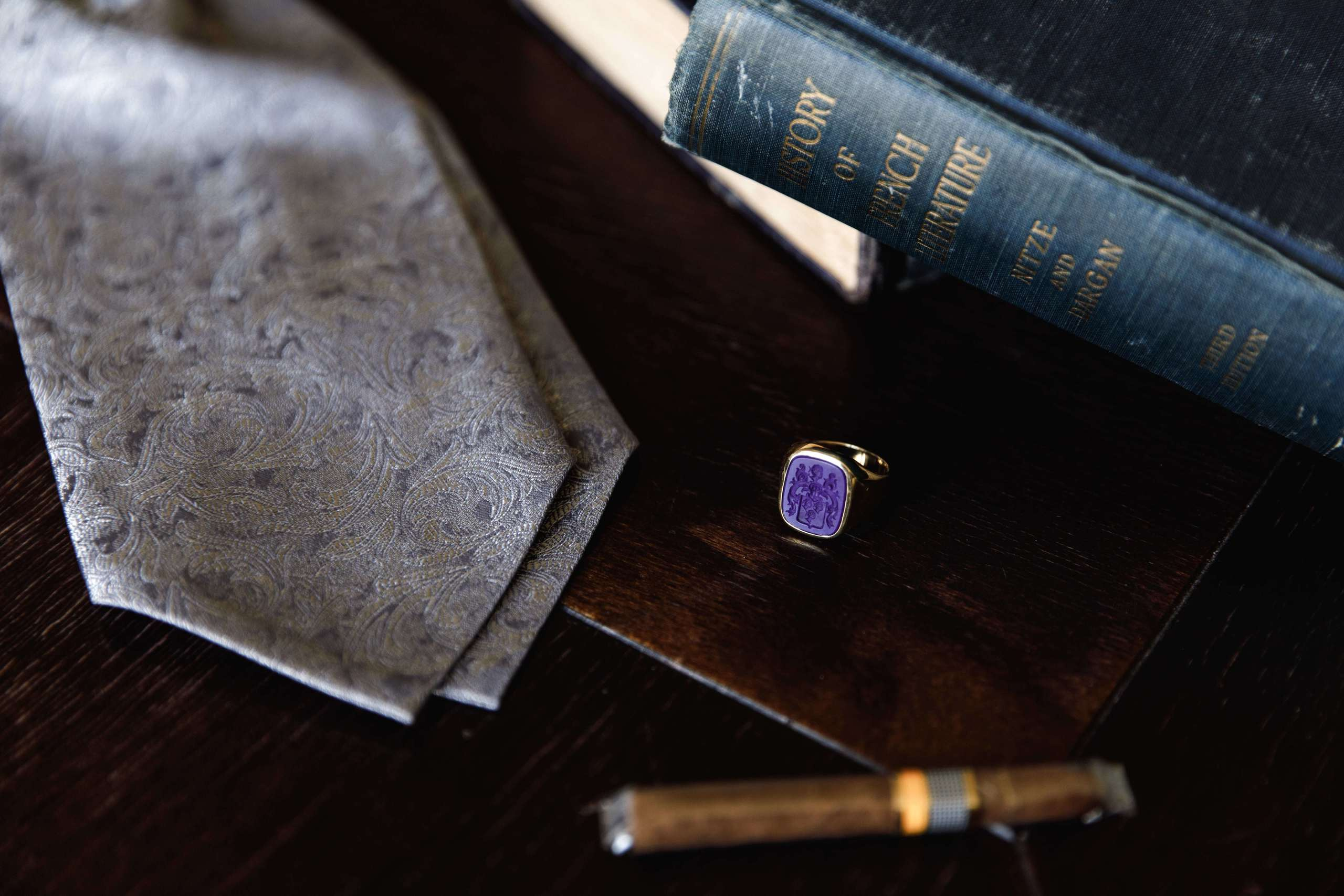 Das Familienring mit Wappen des Bräutigams liegt neben einem alten Buch, einer Zigarre und einer Krawatte.