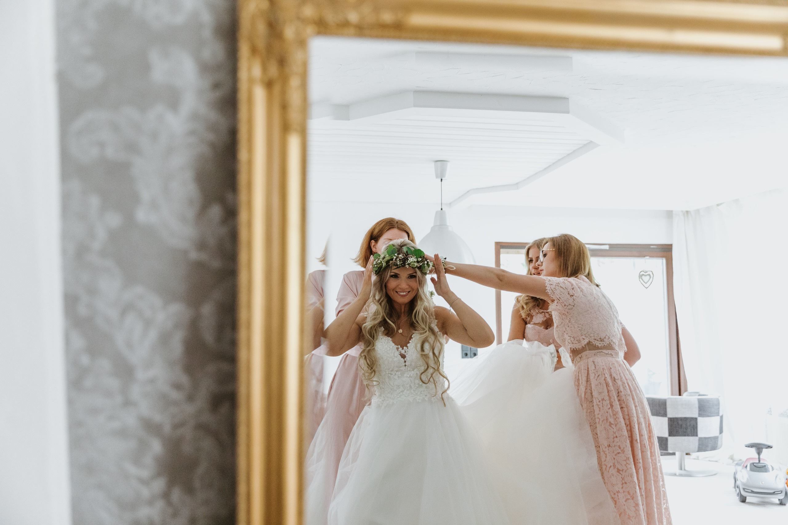 Brautjungfern helfen der Braut, sich fertig zu machen, während alles im Spiegel reflektiert wird.