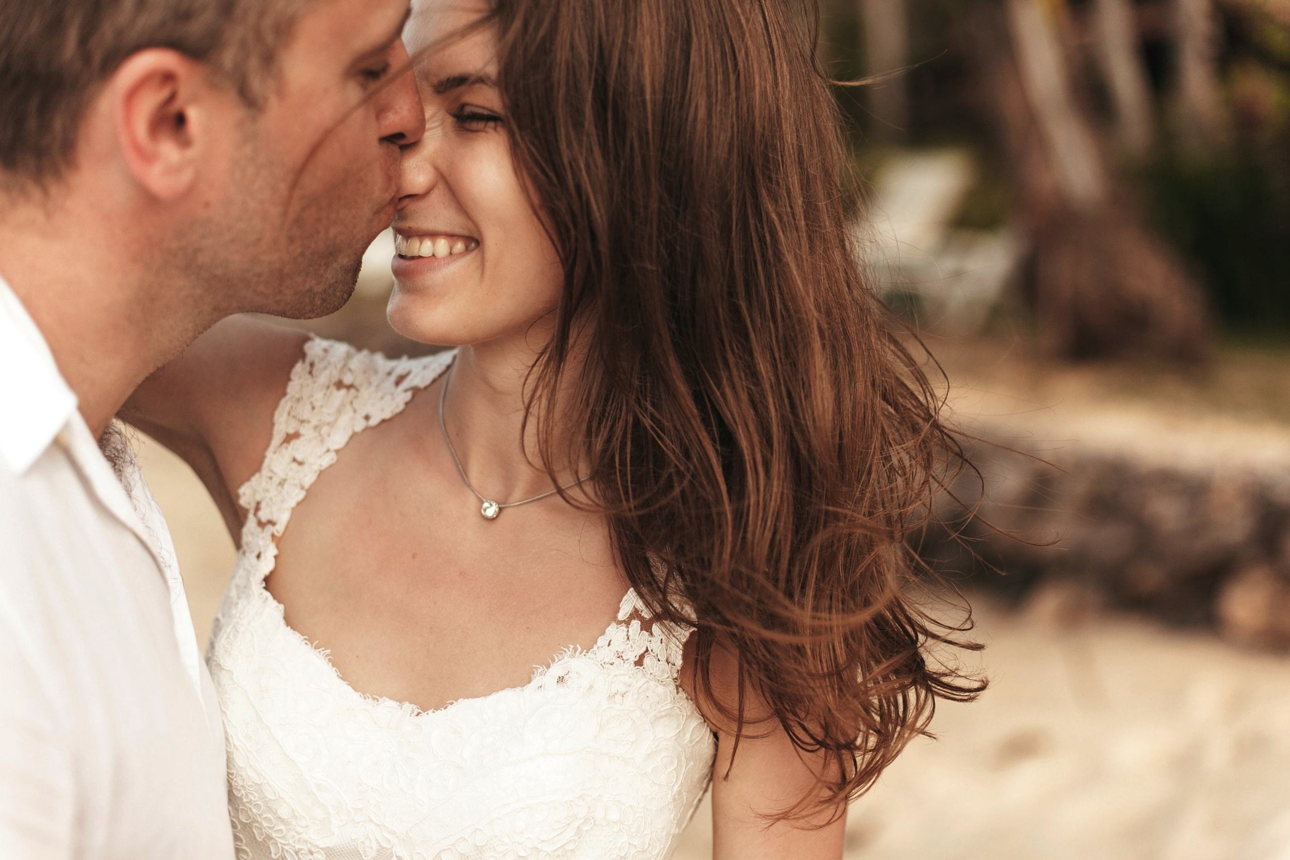 Bräutigam küsst die Braut liebevoll auf die Nase am Strand.