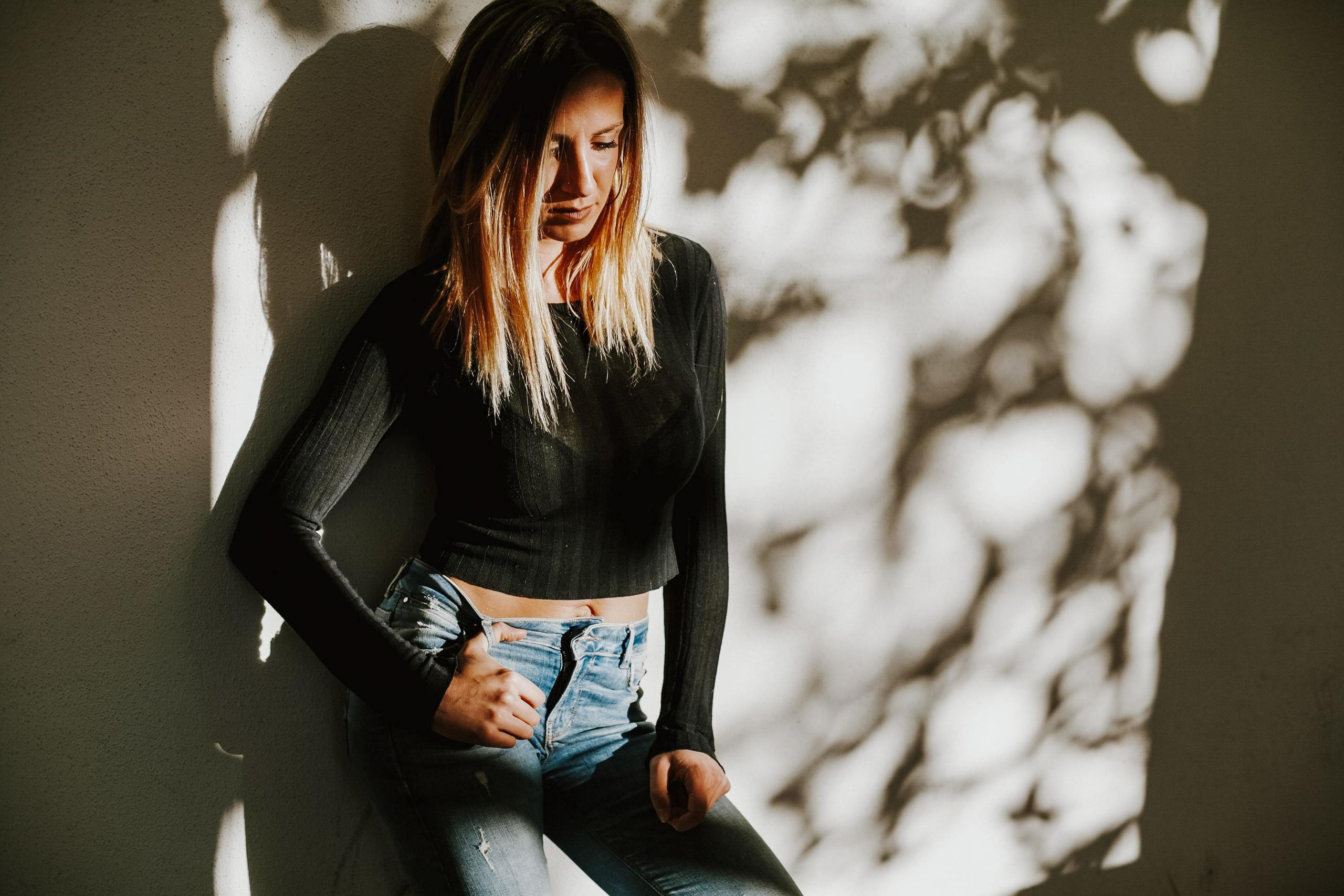 Frau steht an einer Wand im Freien, während zarte Baumschatten ihren Körper umspielen.