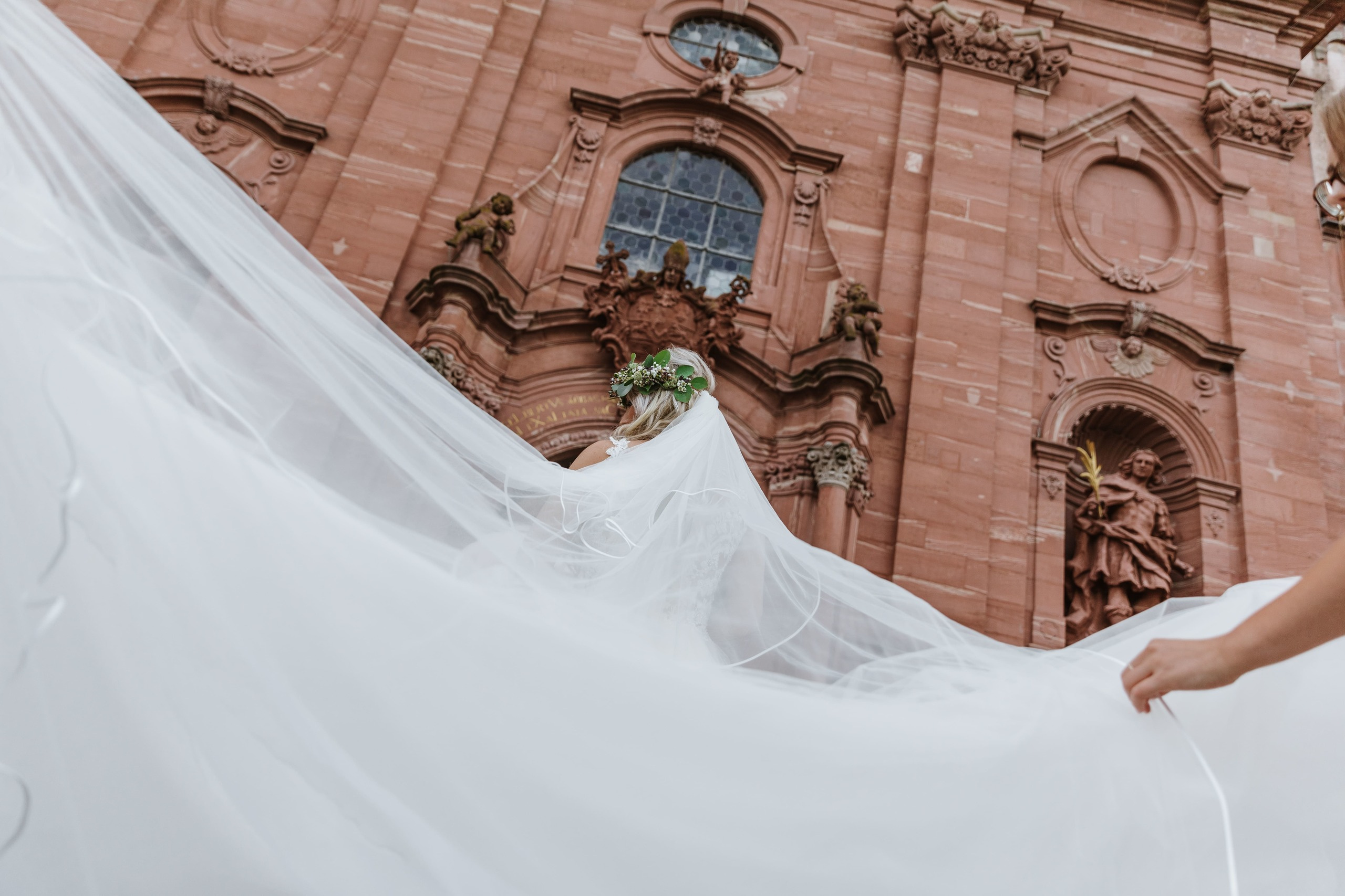 Die Braut geht zur Kirche, während ihre Freundinnen den atemberaubenden Schleier zurechtrücken.