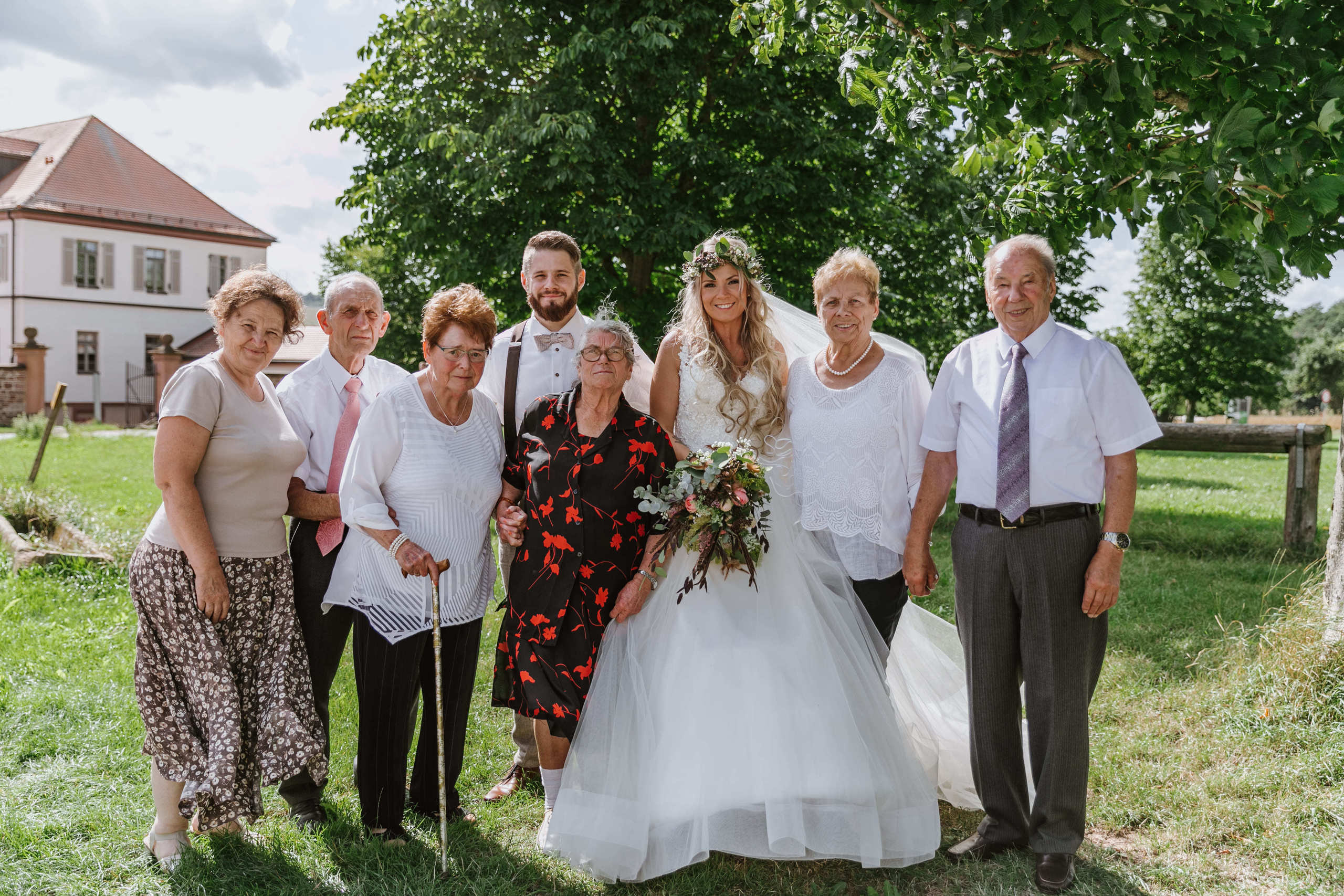 Der Bräutigam und die Braut stehen auf der Wiese mit ihren Großeltern – ein sehr berührender Moment.