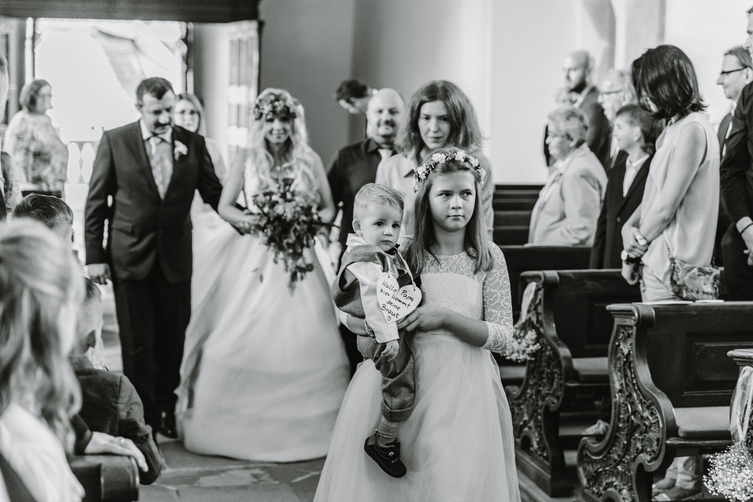 Der Vater begleitet die Braut zum Altar, während Blümenkinder vorausgehen.