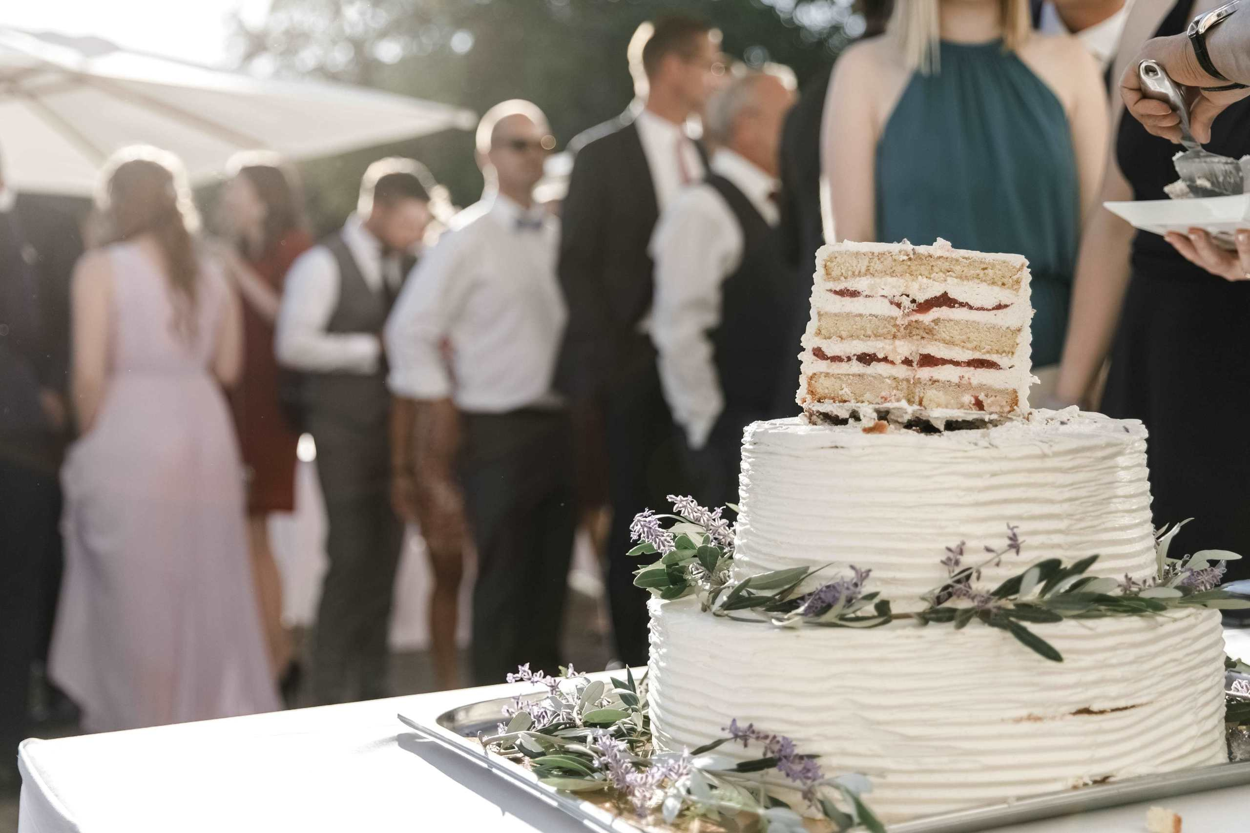 Die Hochzeitstorte steht im Licht der Abendsonne, im Hintergrund sind Gäste zu sehen.