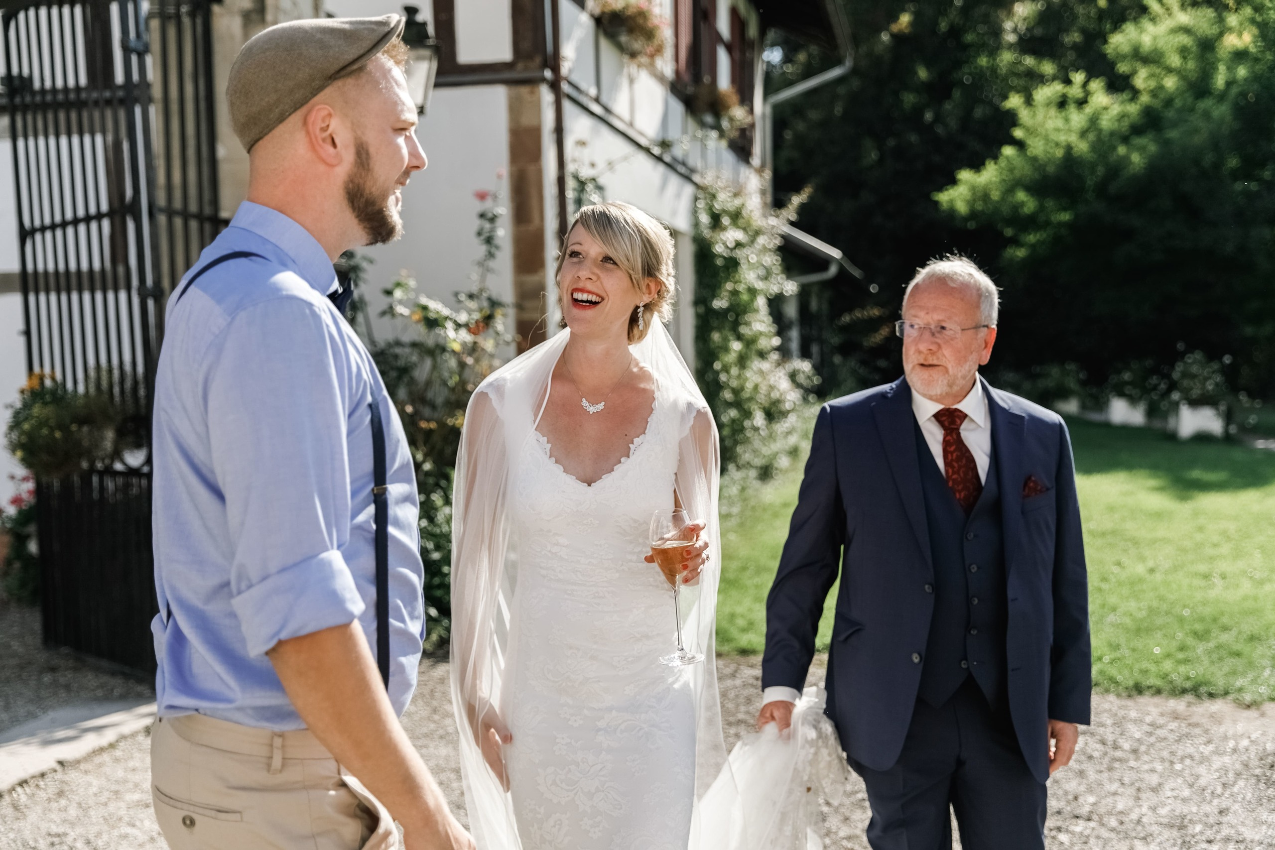 Brautvater hält den Schlepptail des Brautkleides, während die Braut mit einem Gast spricht.