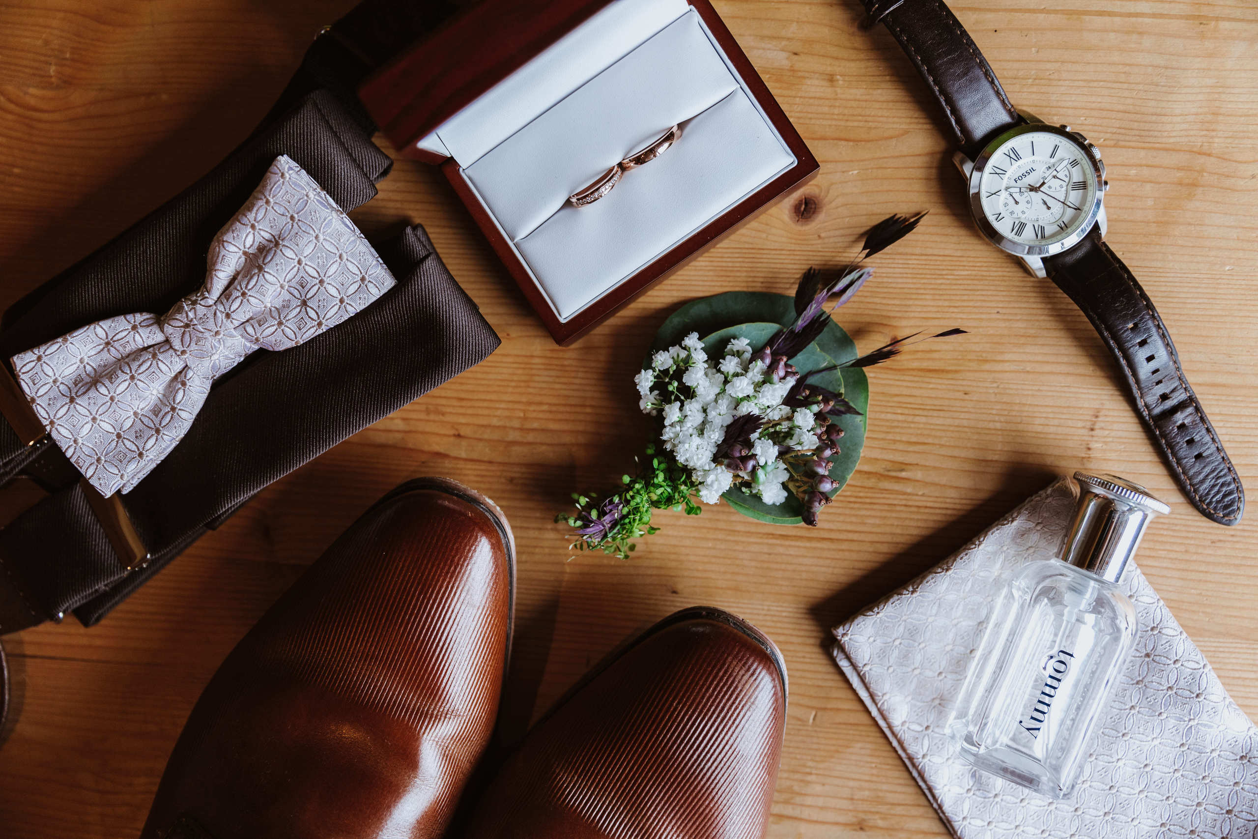Details des Hochzeitsoutfits des Bräutigams – Fliege, Schuhe, Uhr, Blumenboutonnière, Taschentuch und Parfüm.