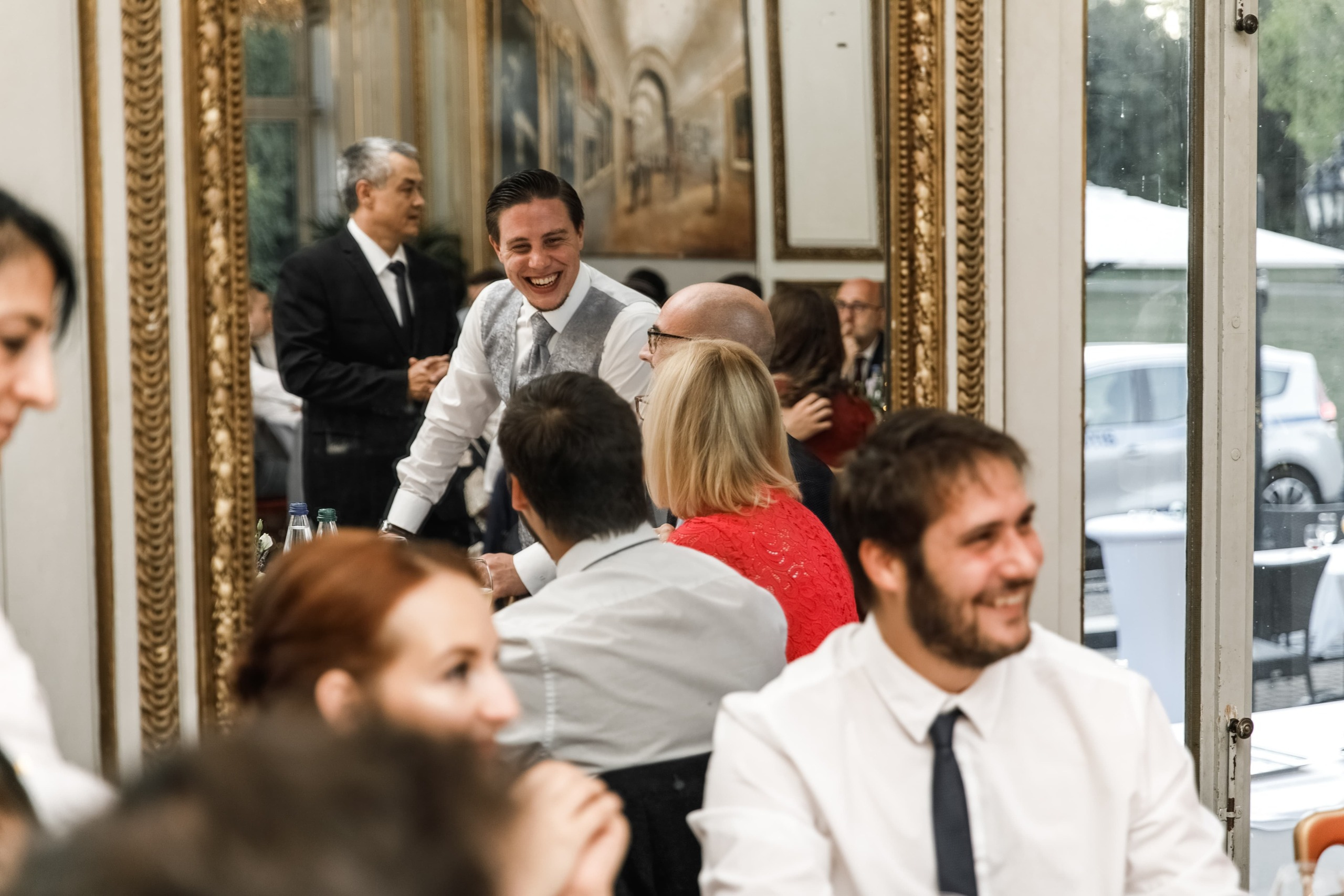 Bräutigam spricht mit Gästen, sichtbar im Spiegel.